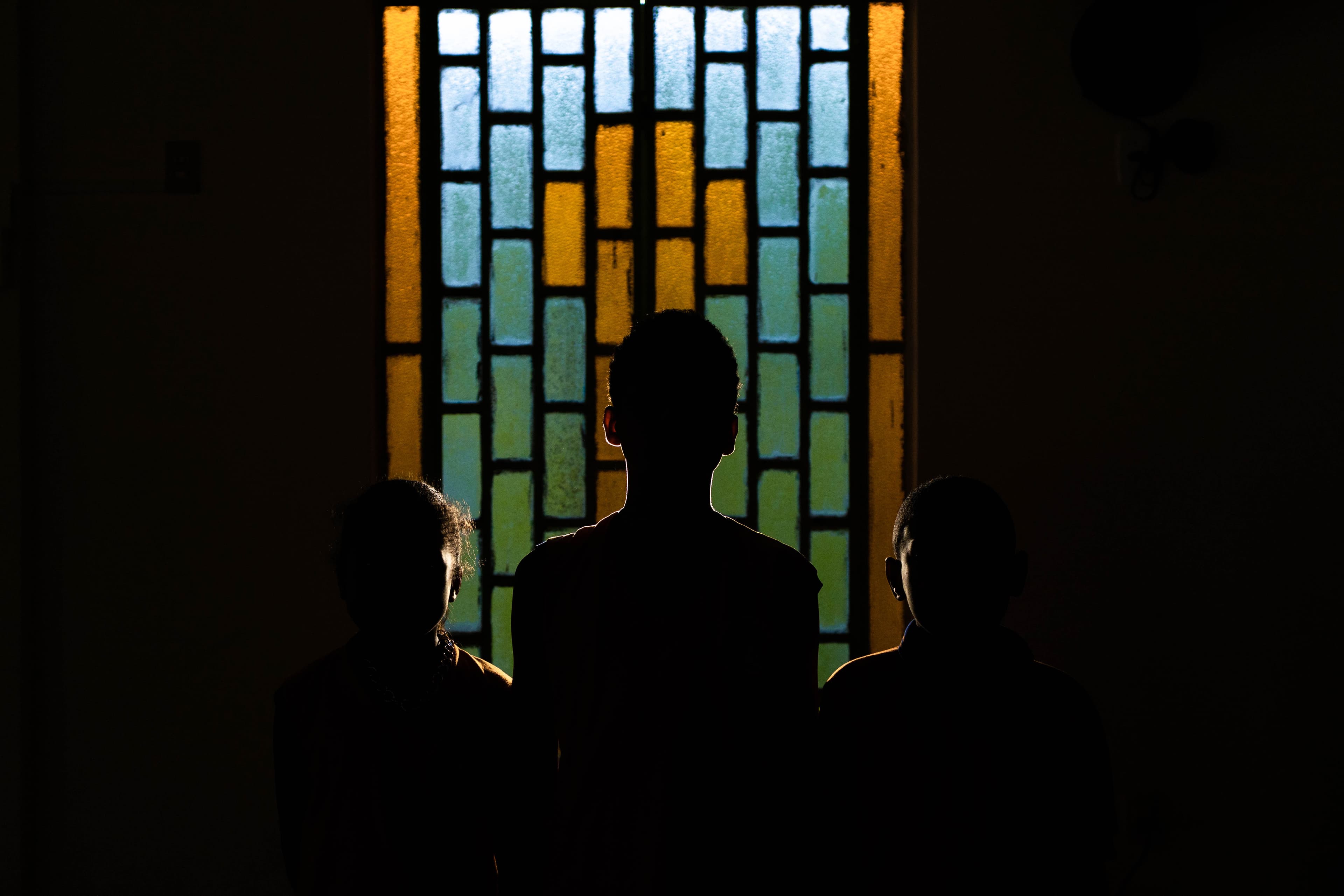 Silhouette of children standing in front of a stained glass window.