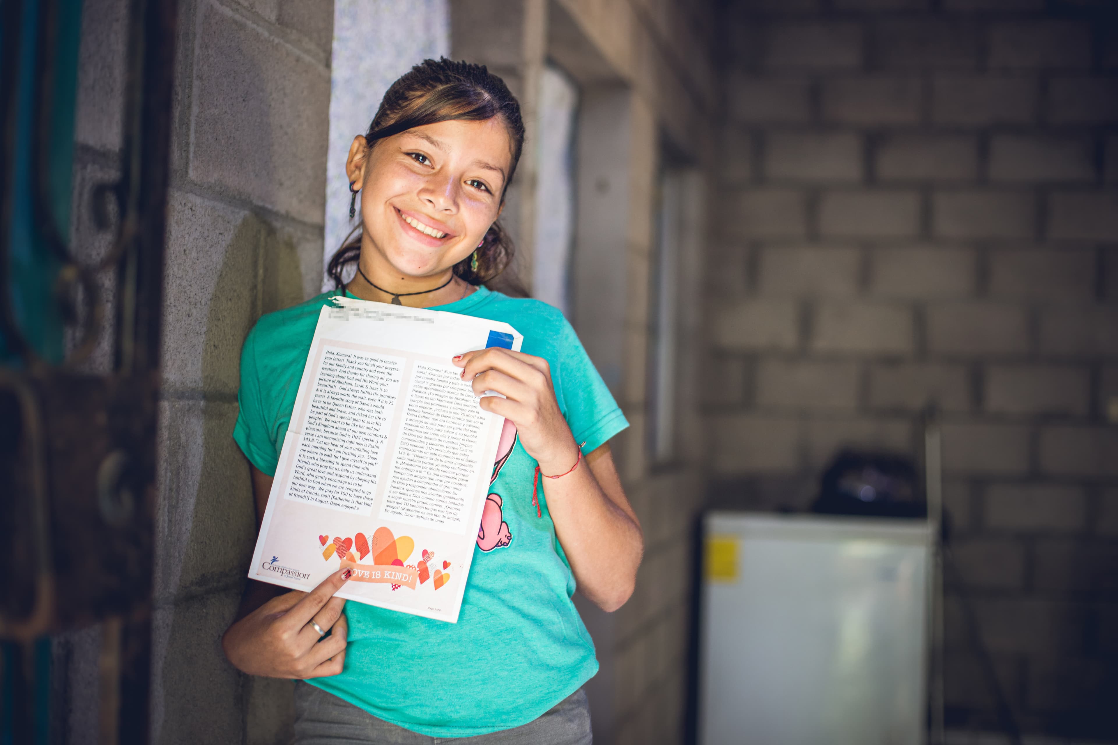 Young girl holds a sponsor letter while smiling.