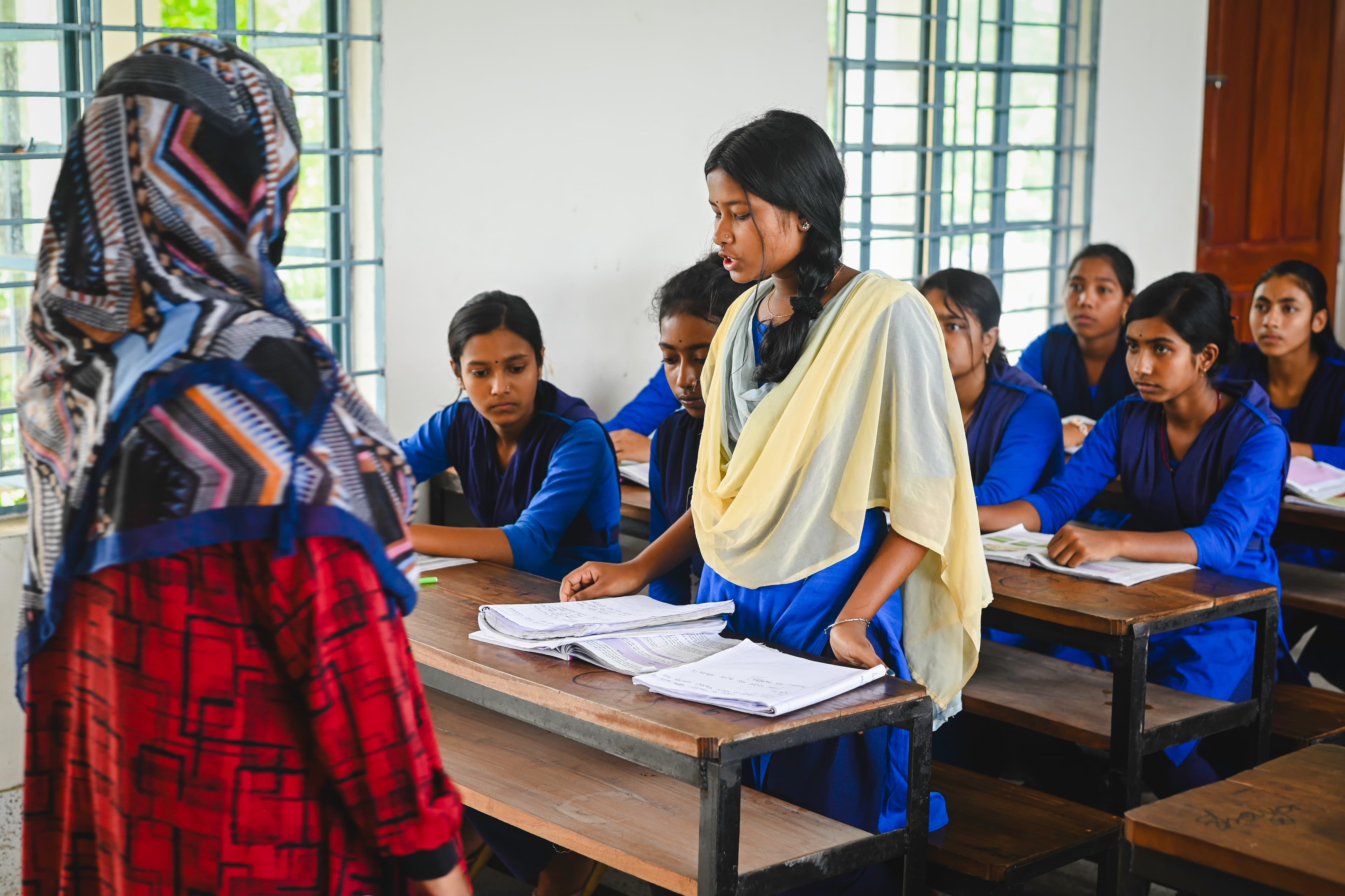 Young woman is standing in a classroom answering a question from her teacher.