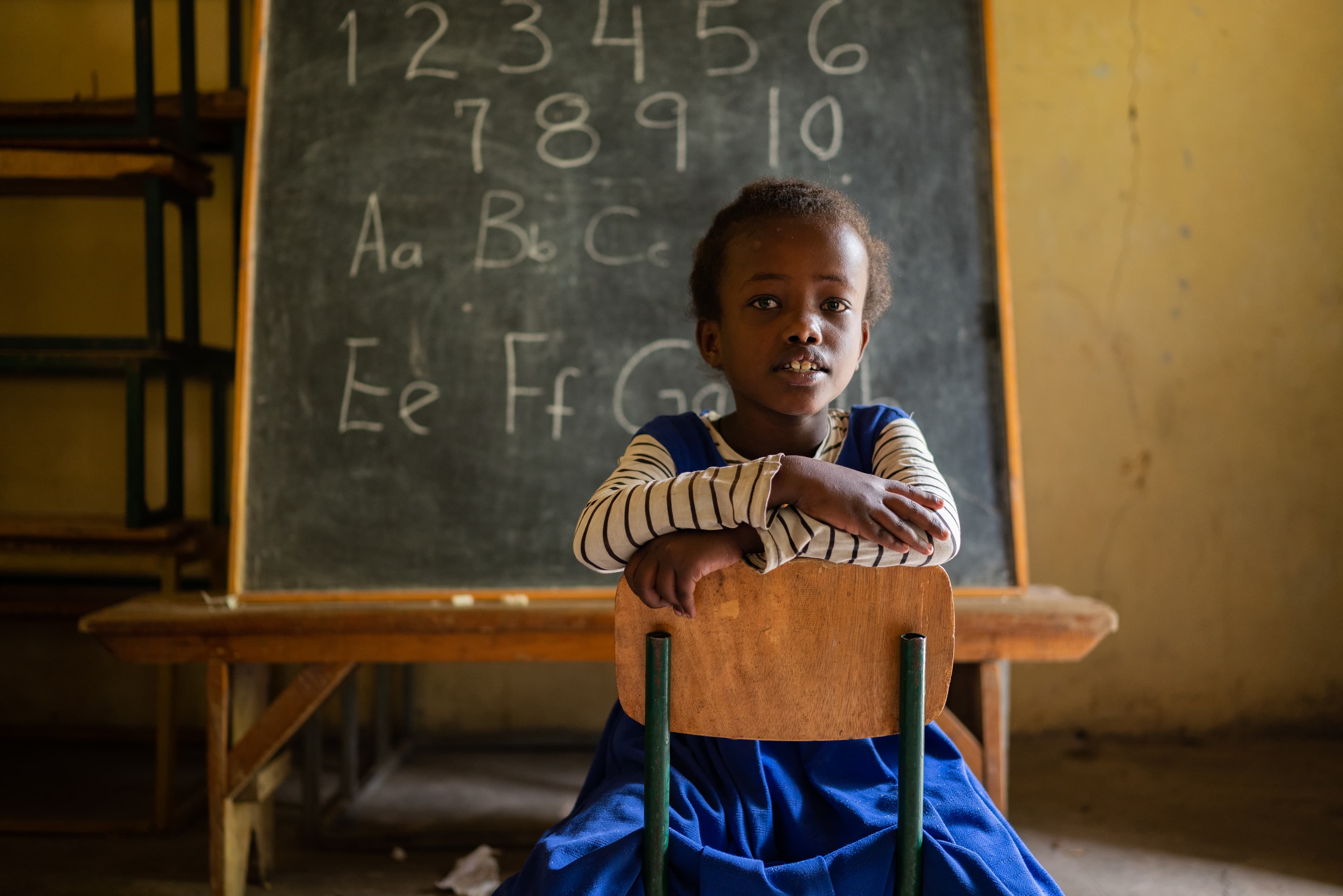 A young girl is sitting in a chair in a classroom with her arms crossed.