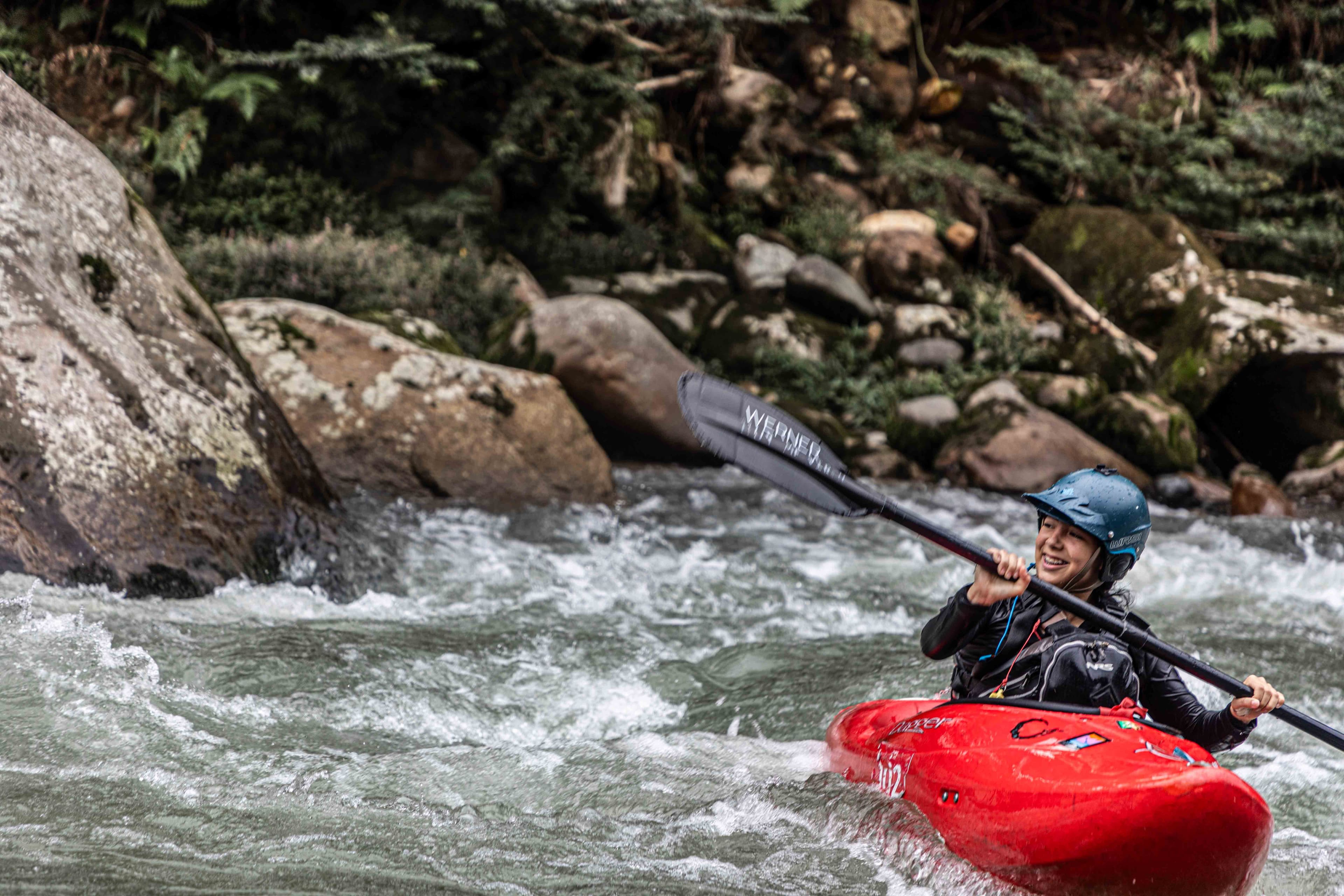 A girl kayaks on rapids in a red kayak.