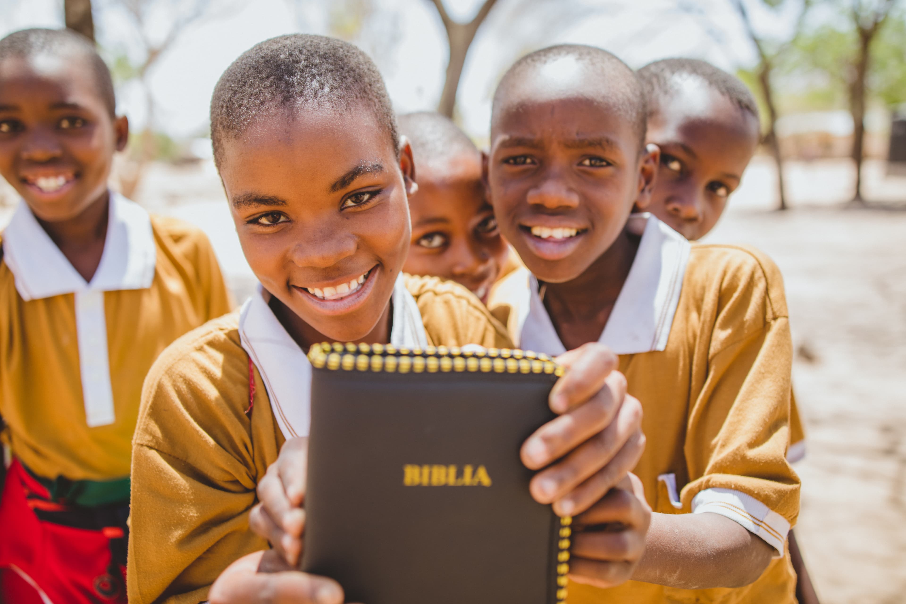 A group of young girls are smiling and holding a bible toward the camera.