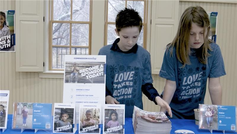 Two kids stand at a table featuring sponsorship booklets and table decor.