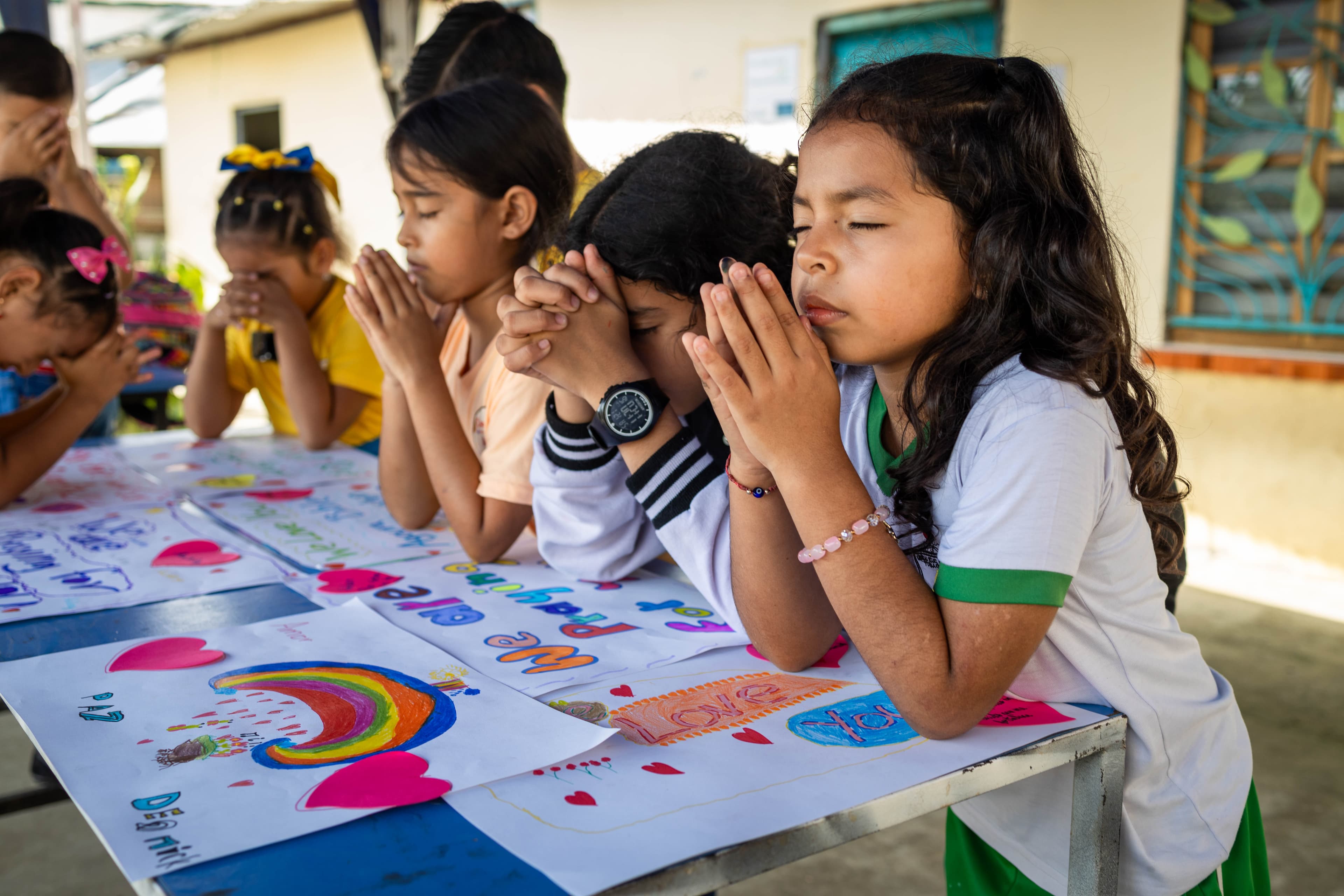 A group of young girls sit at a table with their hands clasped together while praying.