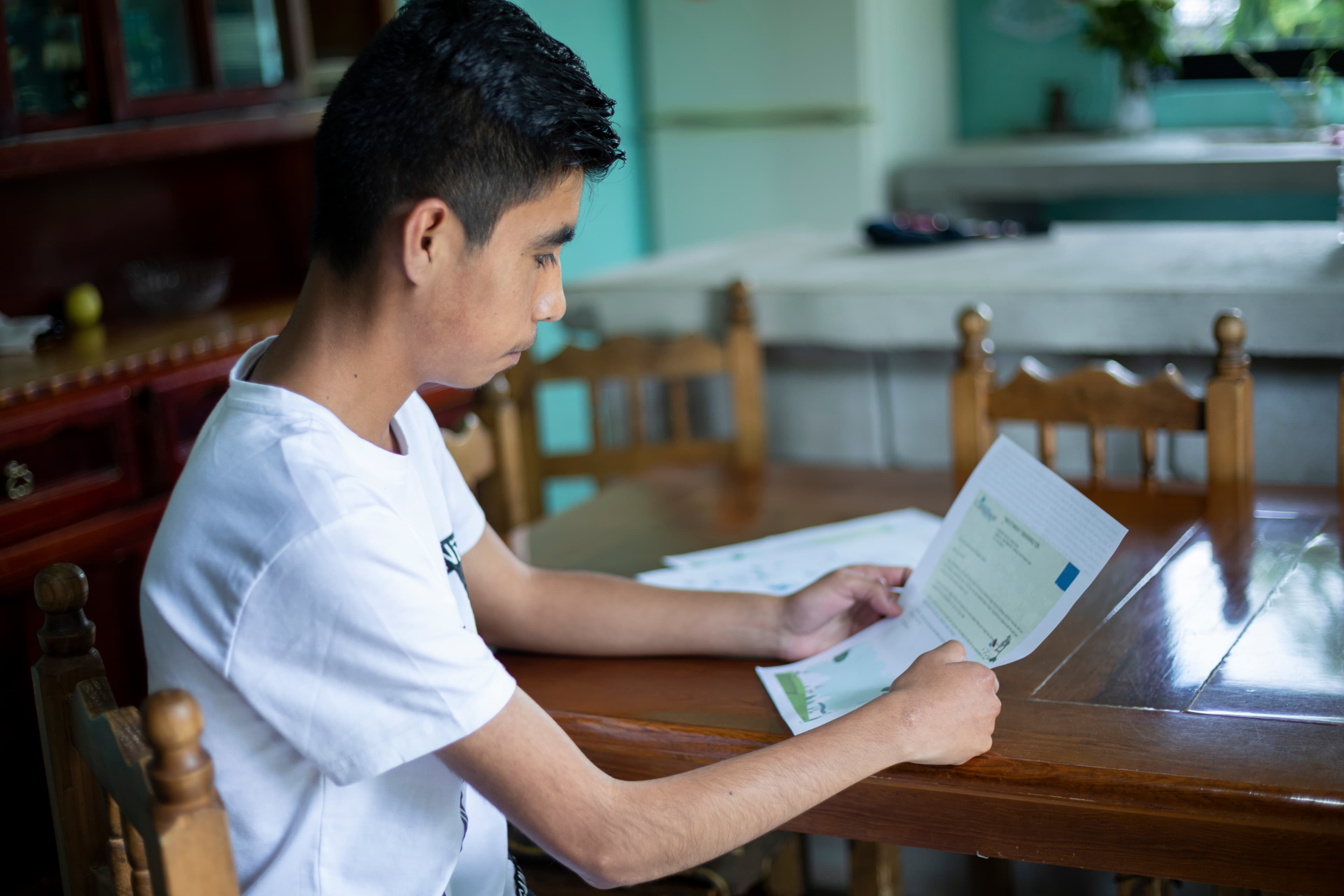 A young man named Yair is sitting at a table reading a letter from his sponsor.