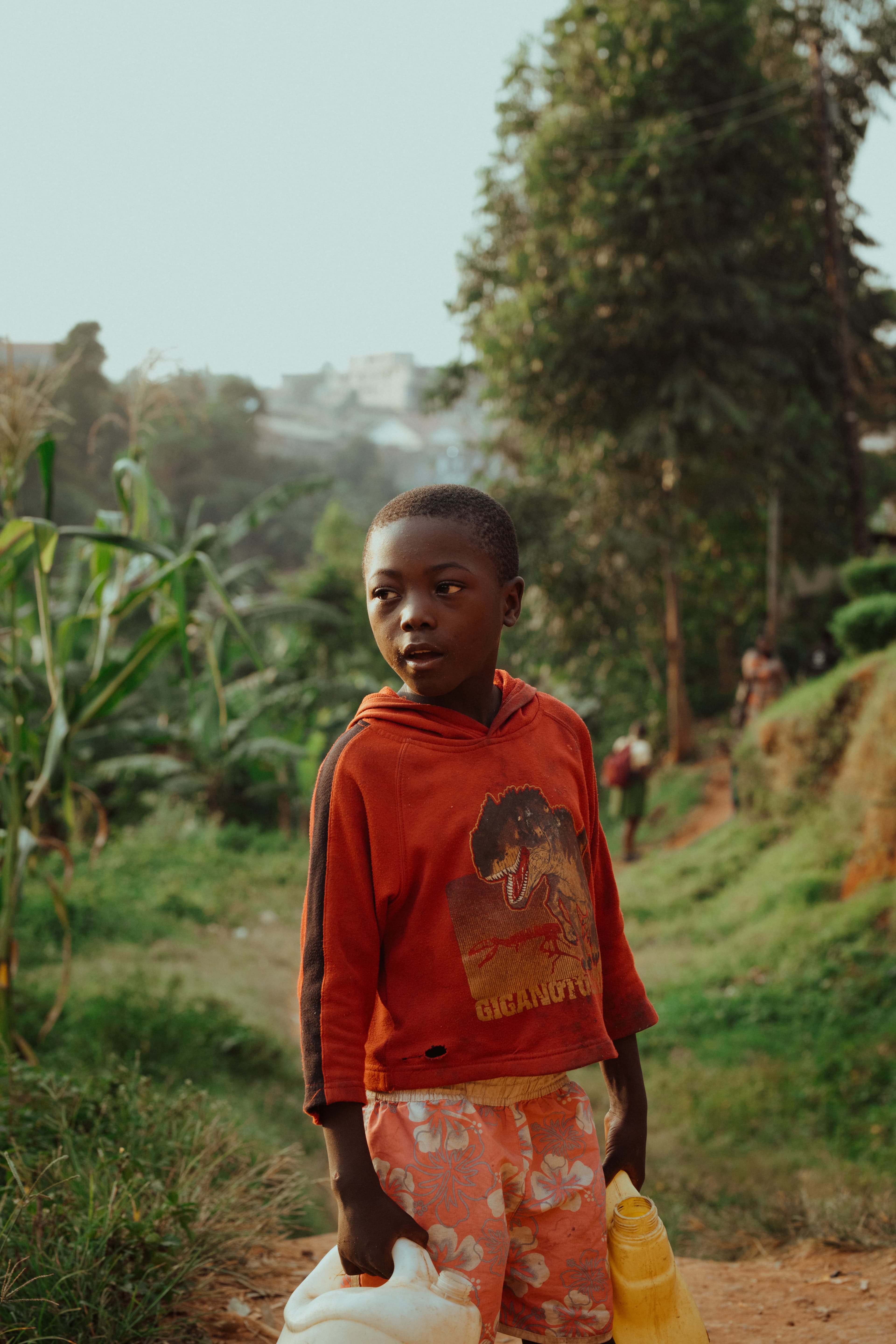 A child walks along a dirt path holding water jugs.