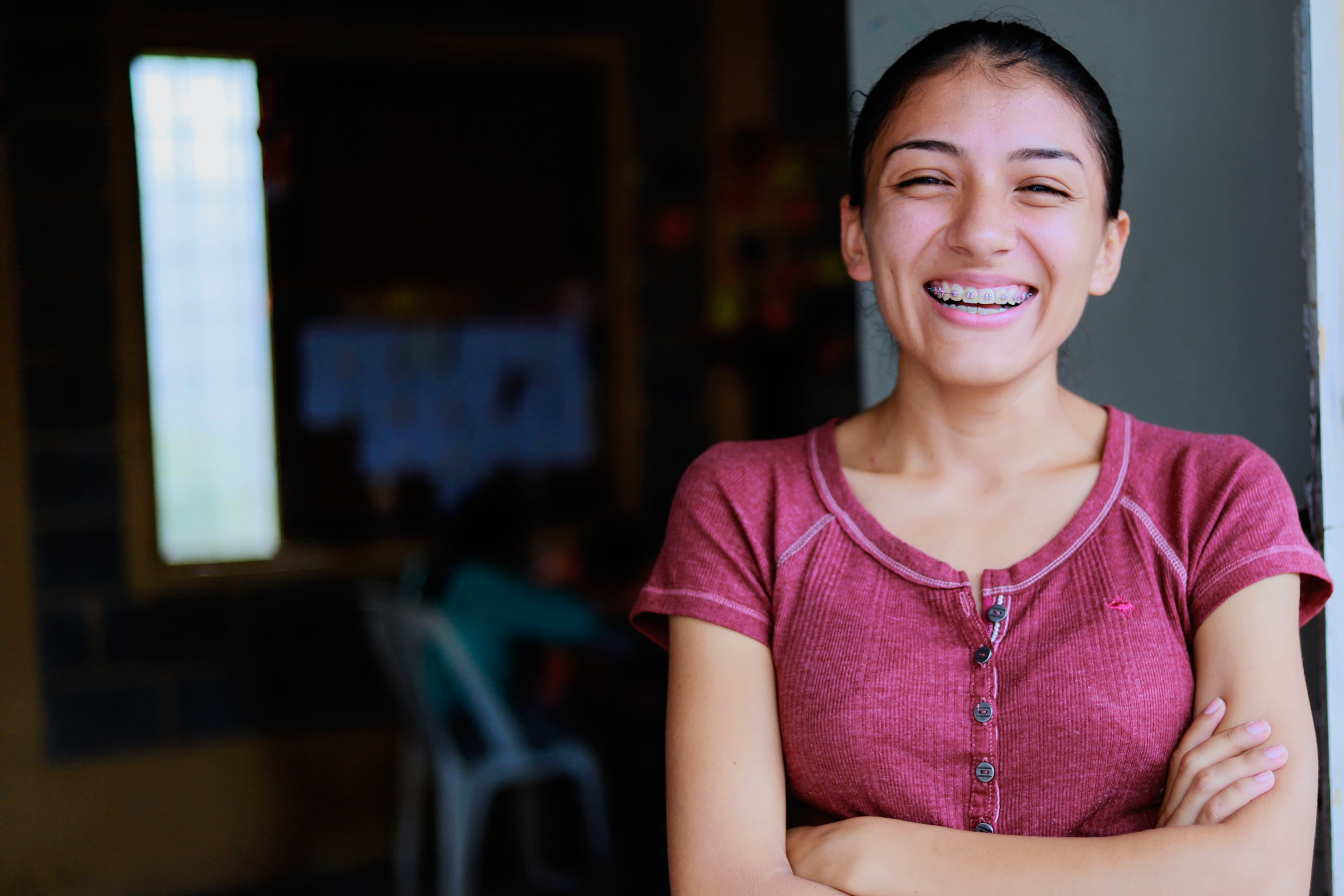 A young woman smiles bright at the camera. She has braces and is wearing a red shirt.