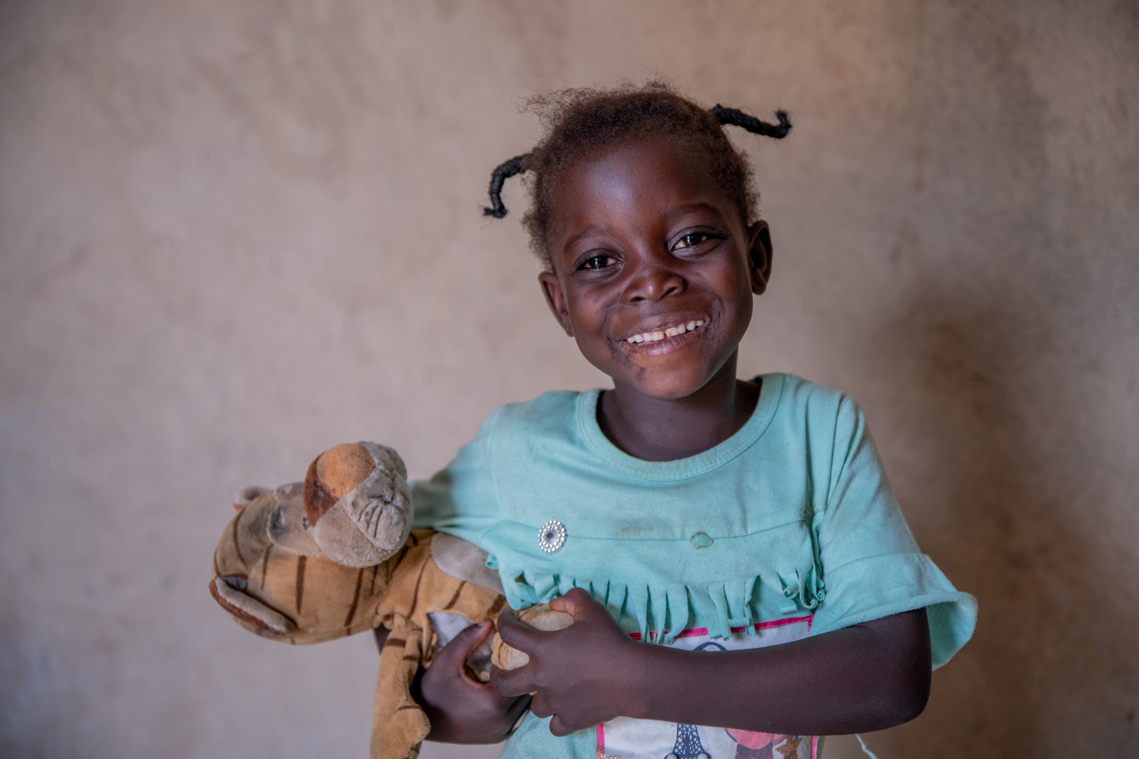 A young African girl holds a stuffed animal while smiling for the camera.