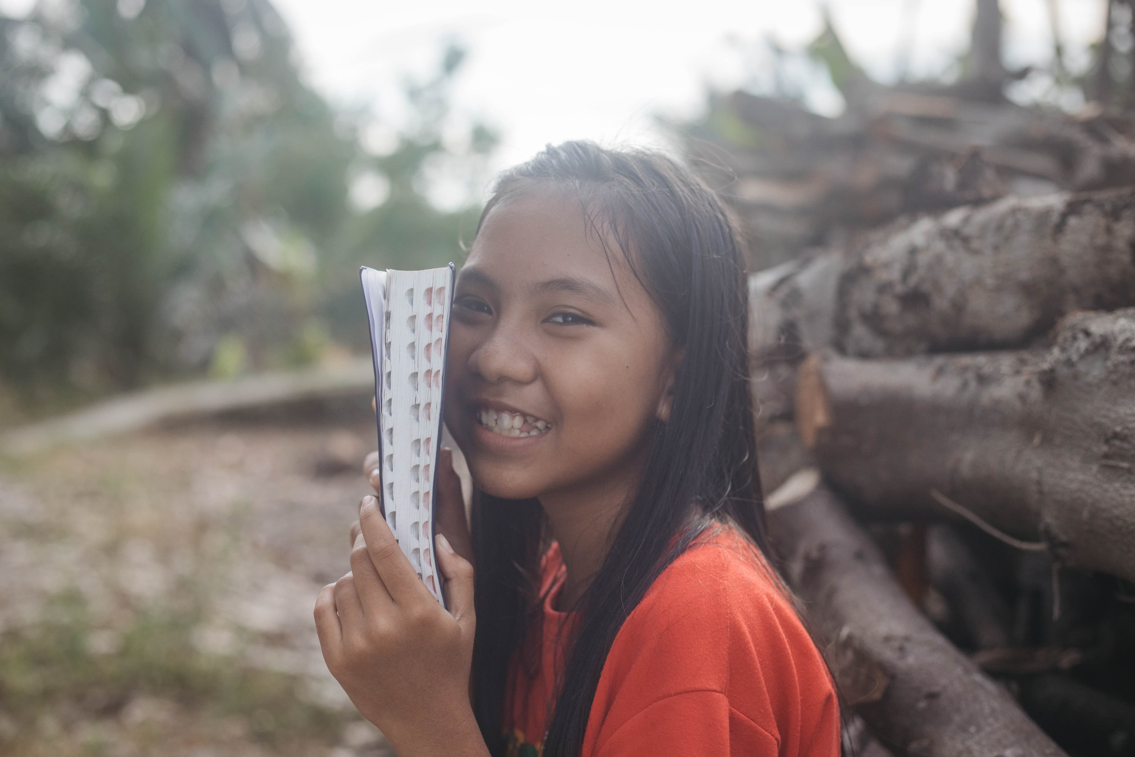 A young girl holds a bible next to her face as she smiles.
