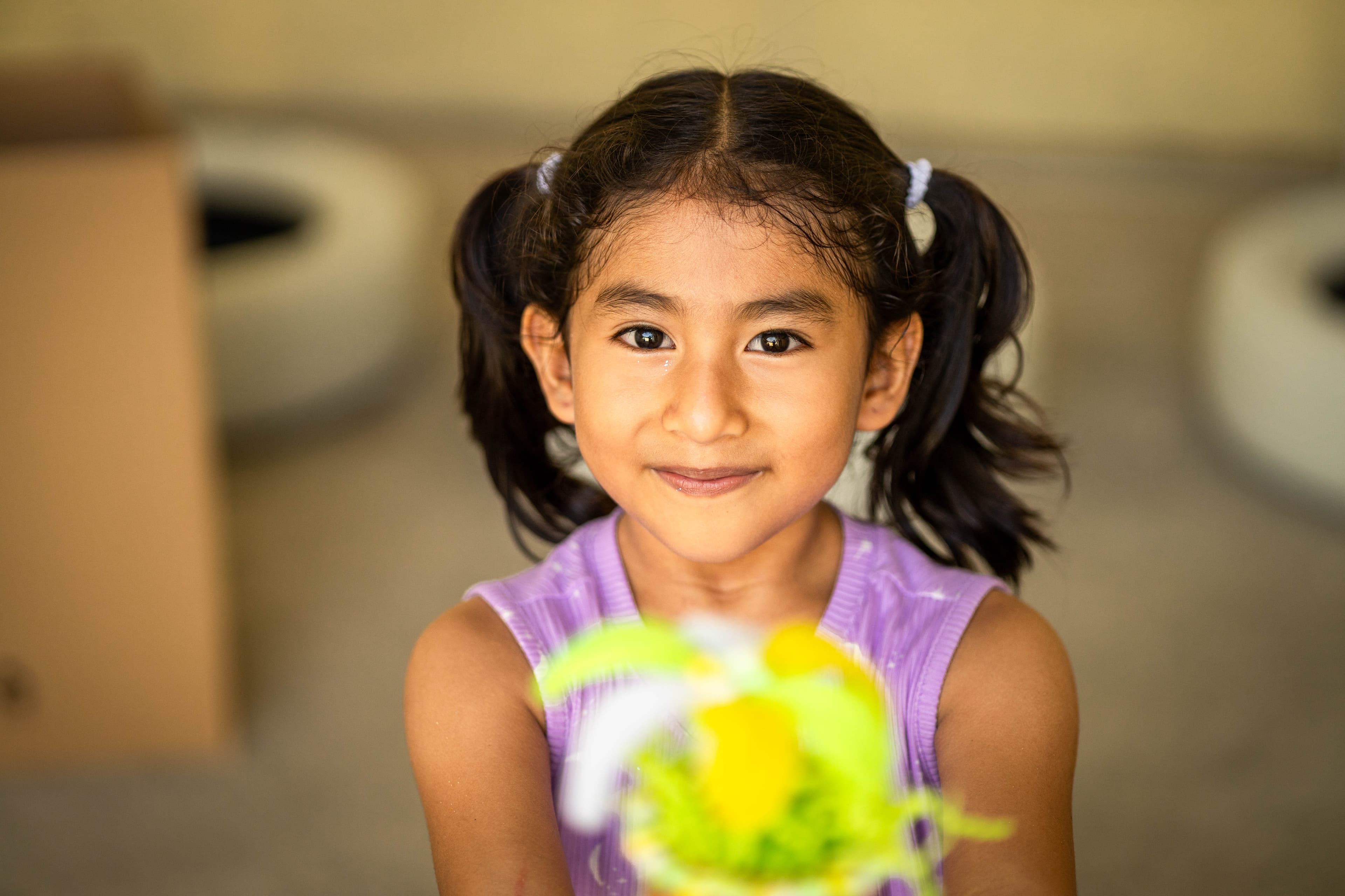 A 6 year old girl named Luana is at the centre, holding her vase in front of her. She is smiling in this portrait and the vase is blurred by lens bokeh.