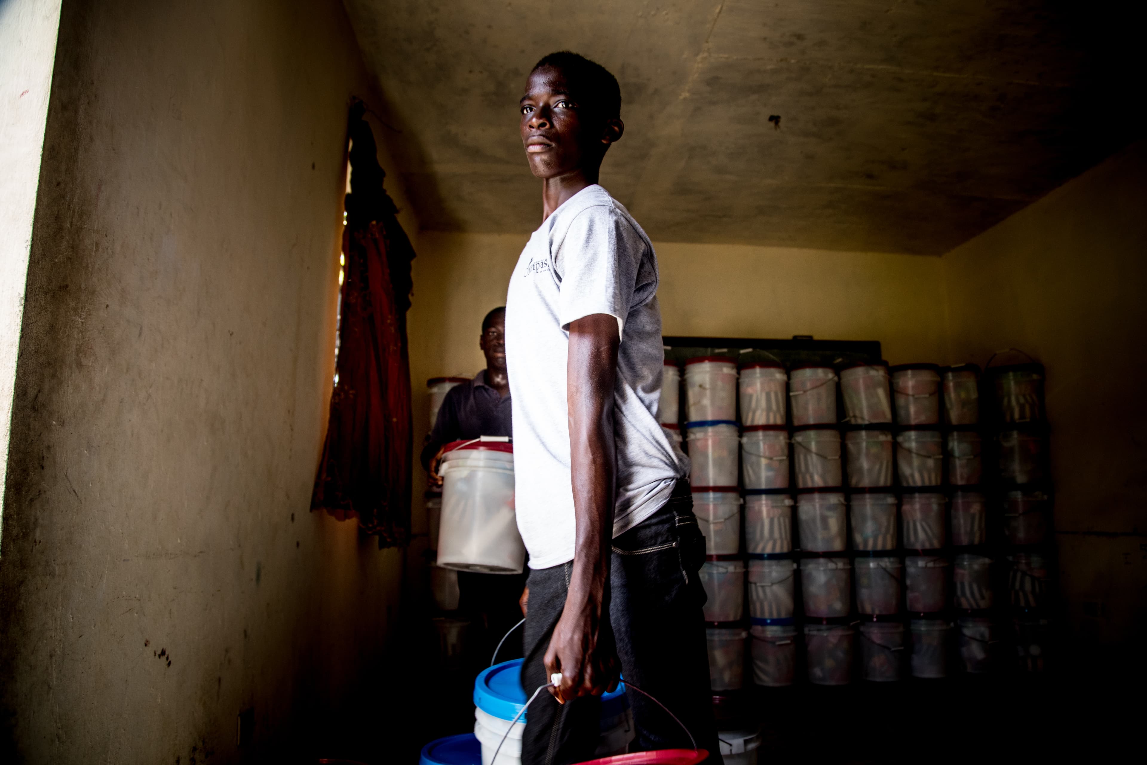Young man is standing in a dark room holding a bucket in his hands, delivering relief resources to a local community.