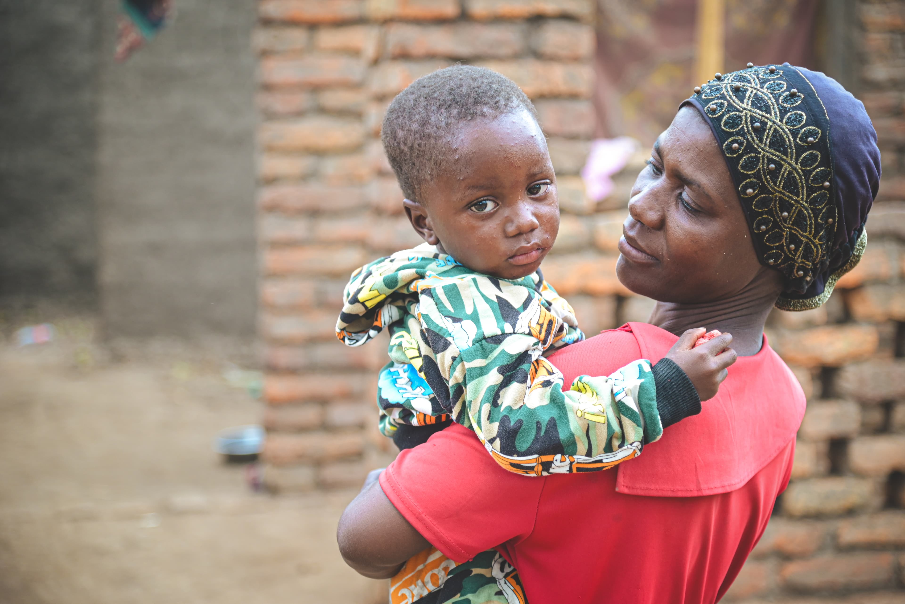 An African mom holds her toddler son as he looks at the camera.