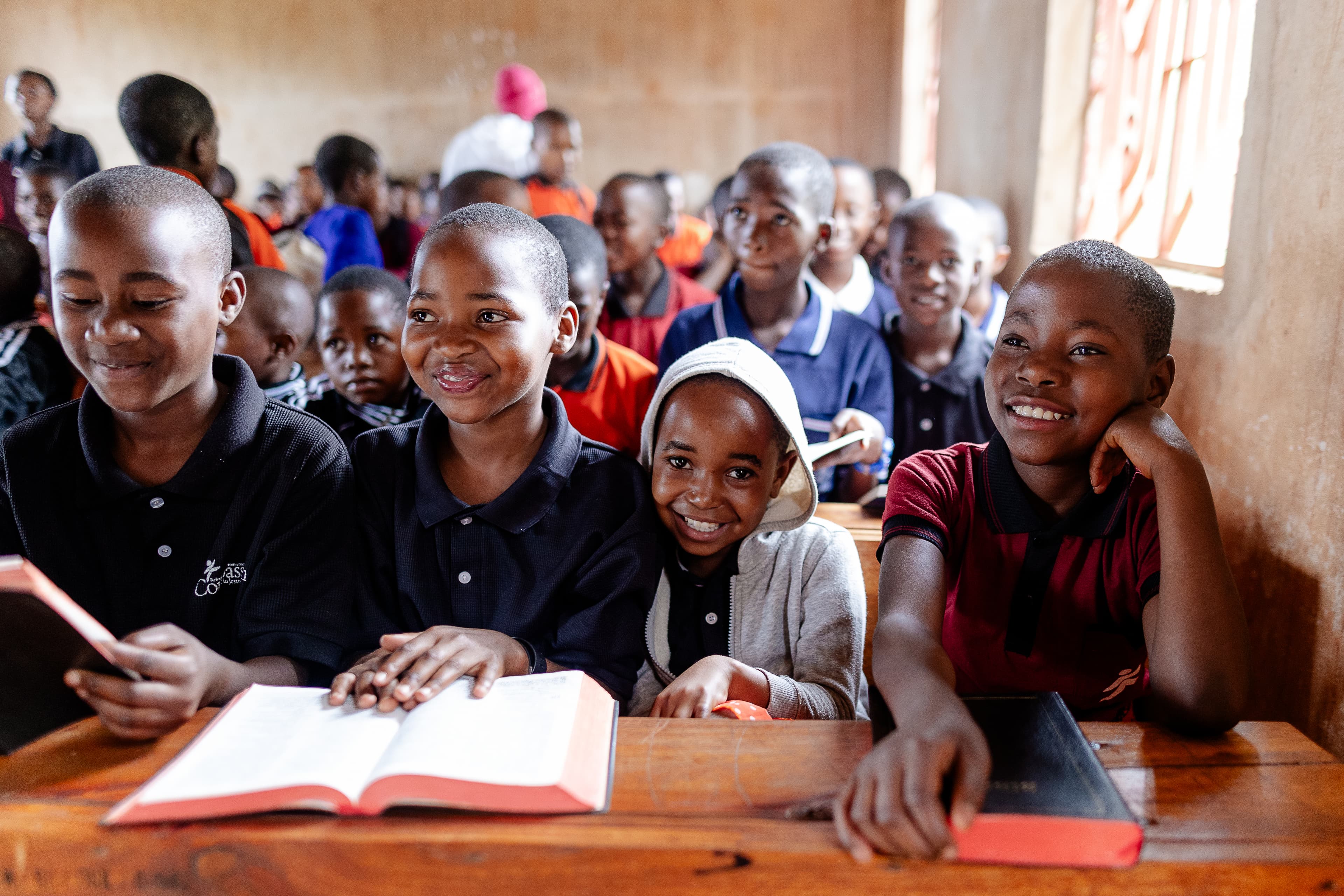 Children smile while opening their Bibles in a classroom filled with children.
