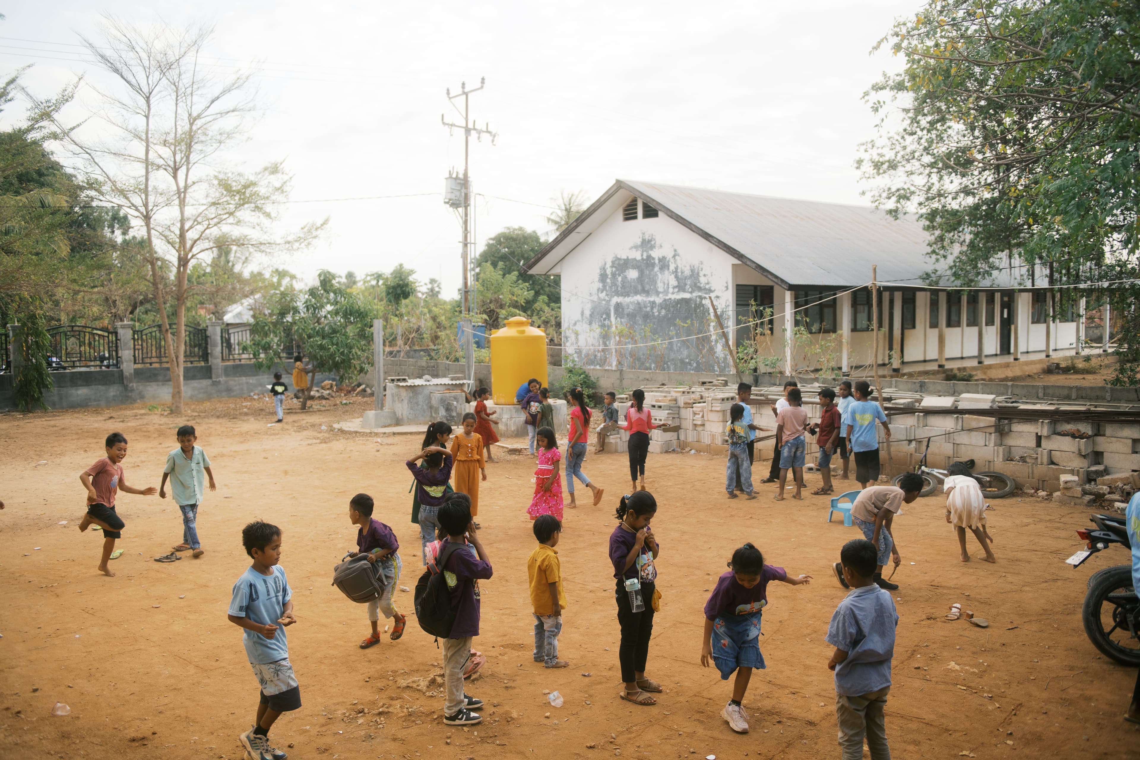 A group of Indonesian children play in a dirt yard outside of a building.