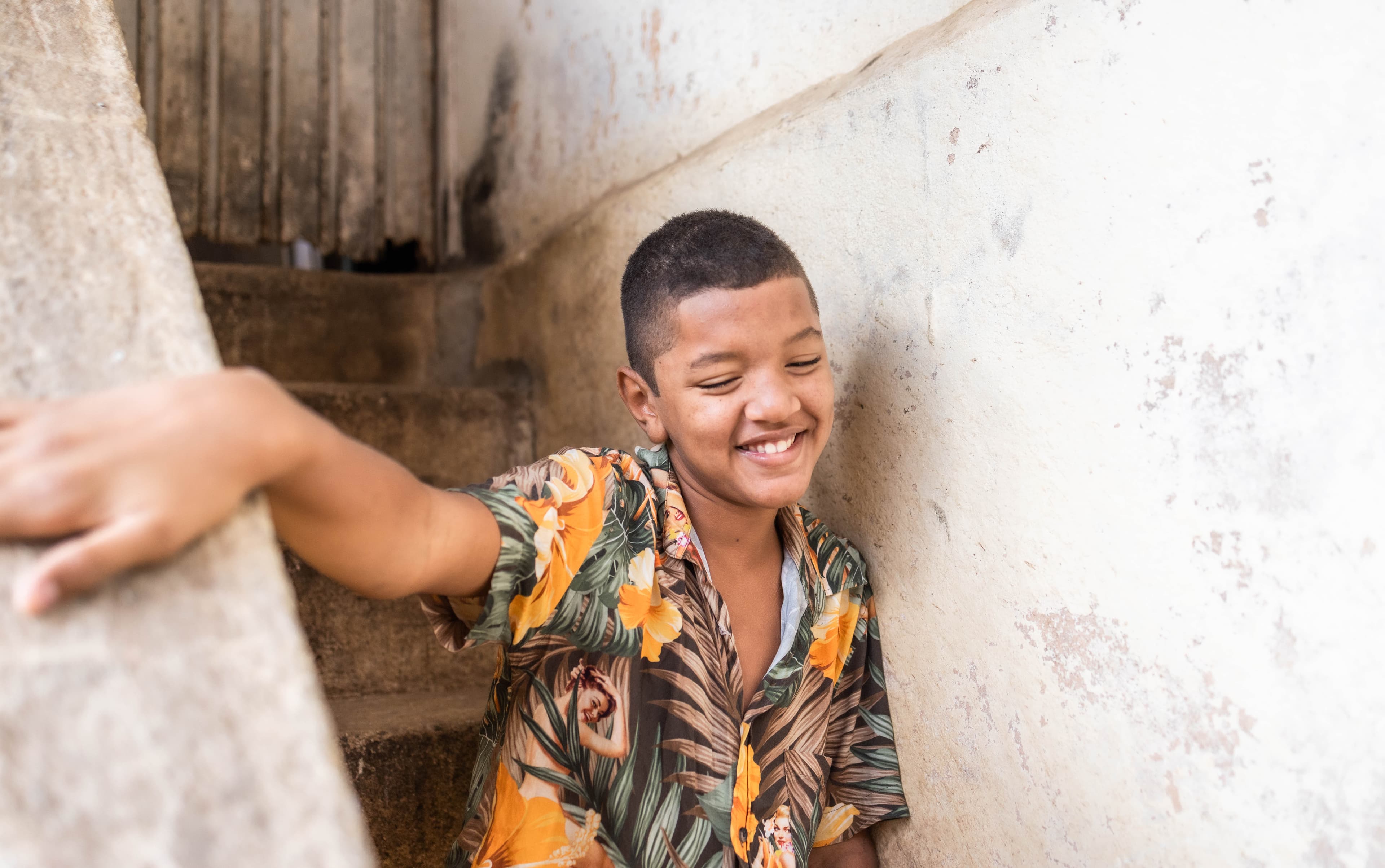 A teen boy wearing a floral shirt smiles.