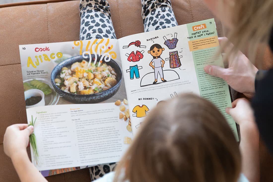 A young girl sits on the couch with her mom reading Compassion's Explorer Magazine.