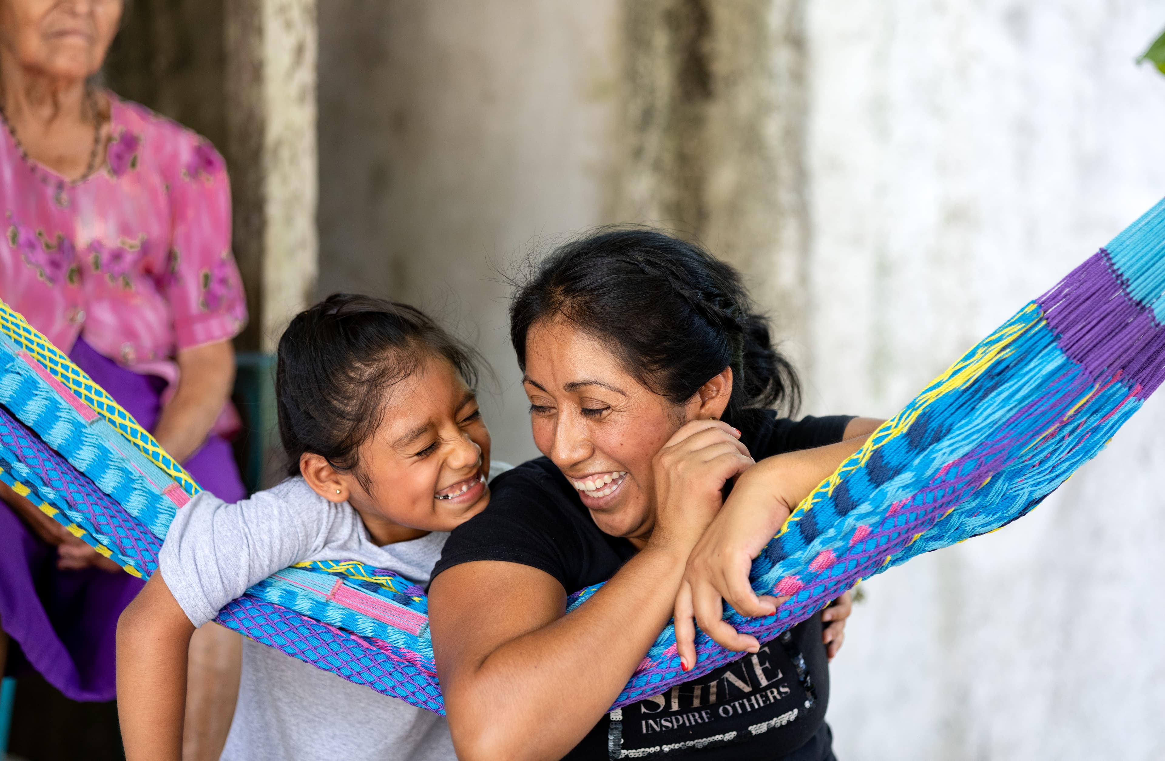 A mother and child are laughing as they lean on a colorful hammock.