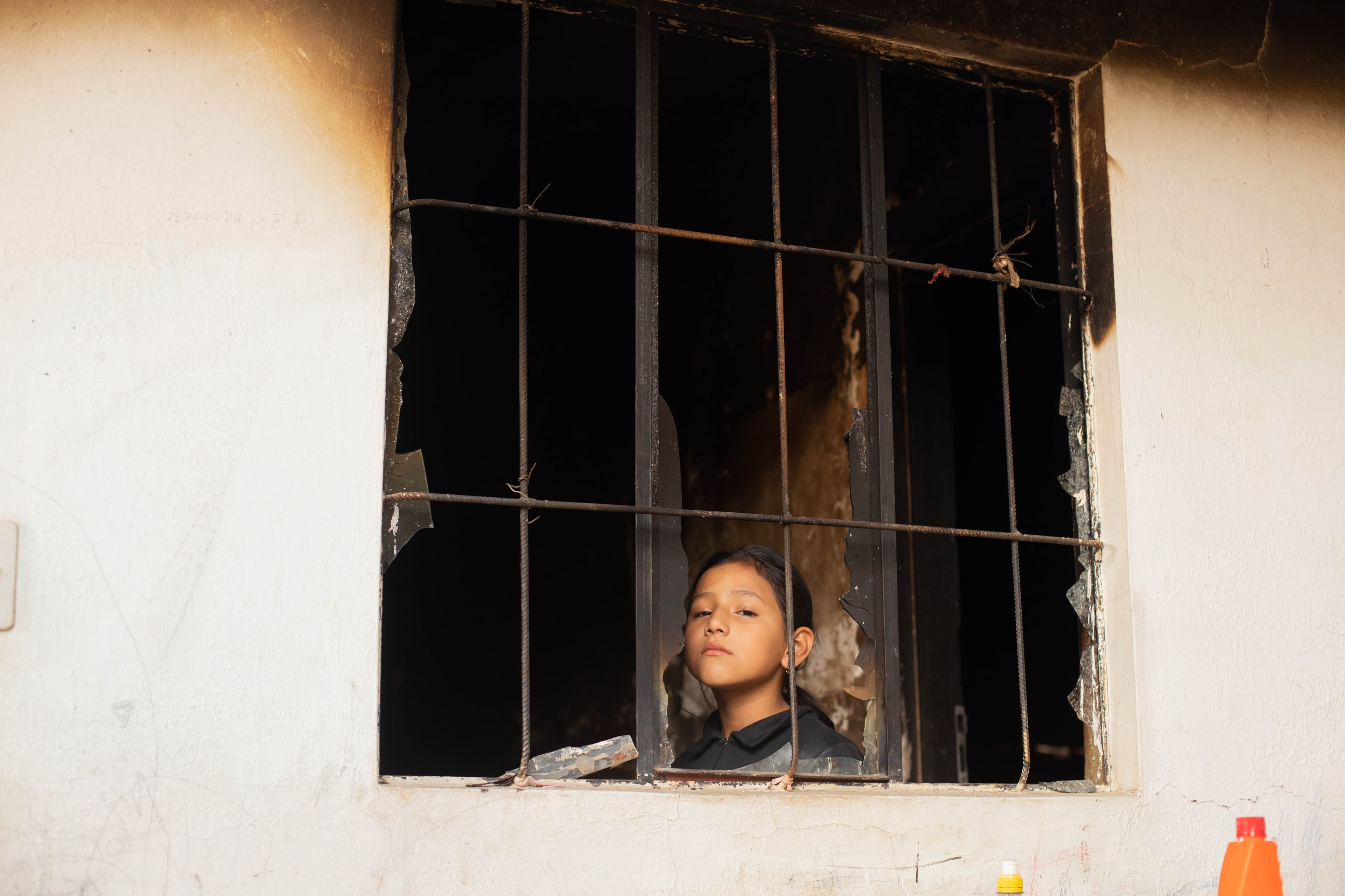 A teen girl looks out a broken window.