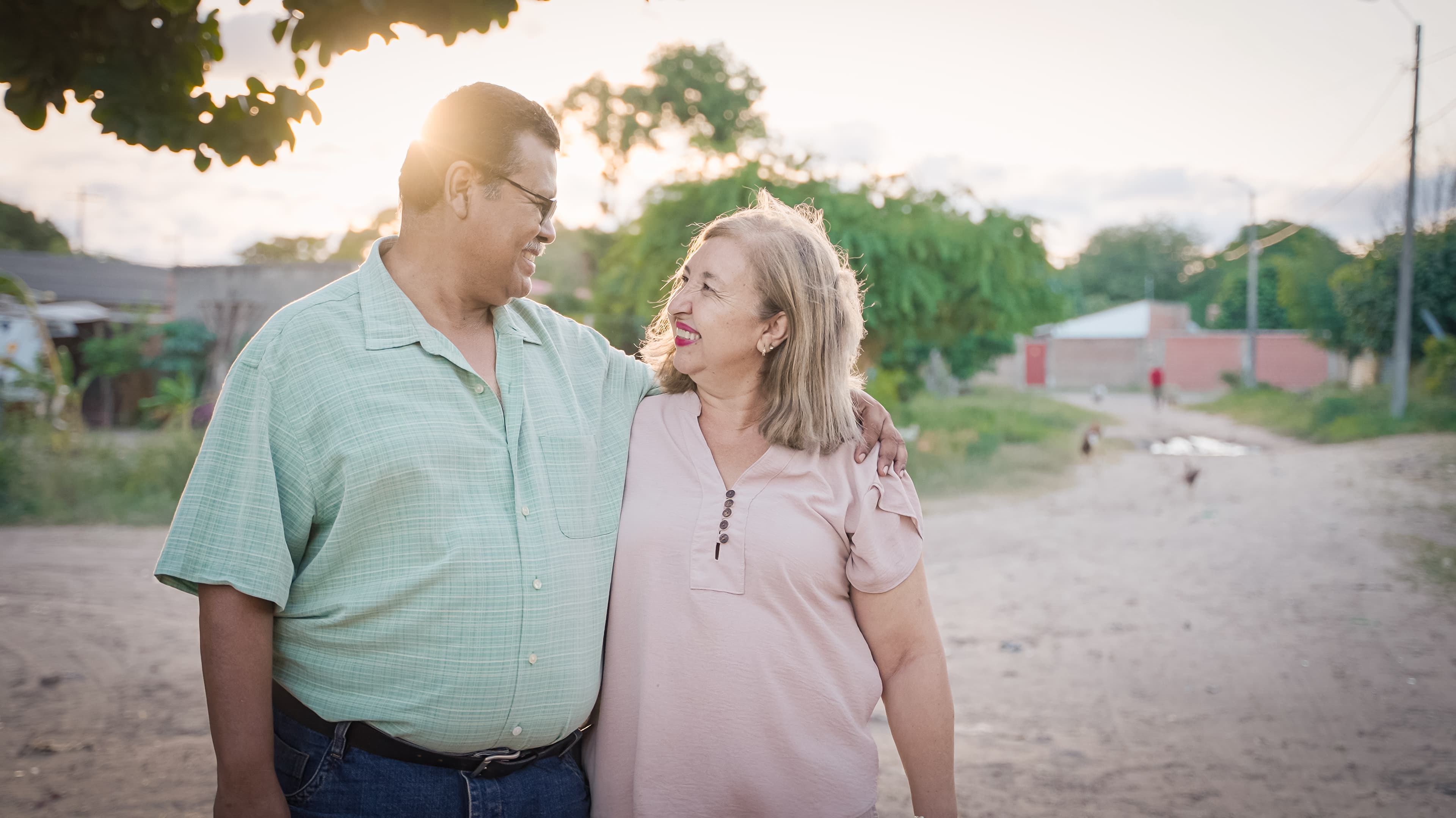 A man wearing a green shirt and a woman wearing a pink shirt look at each other and smile.