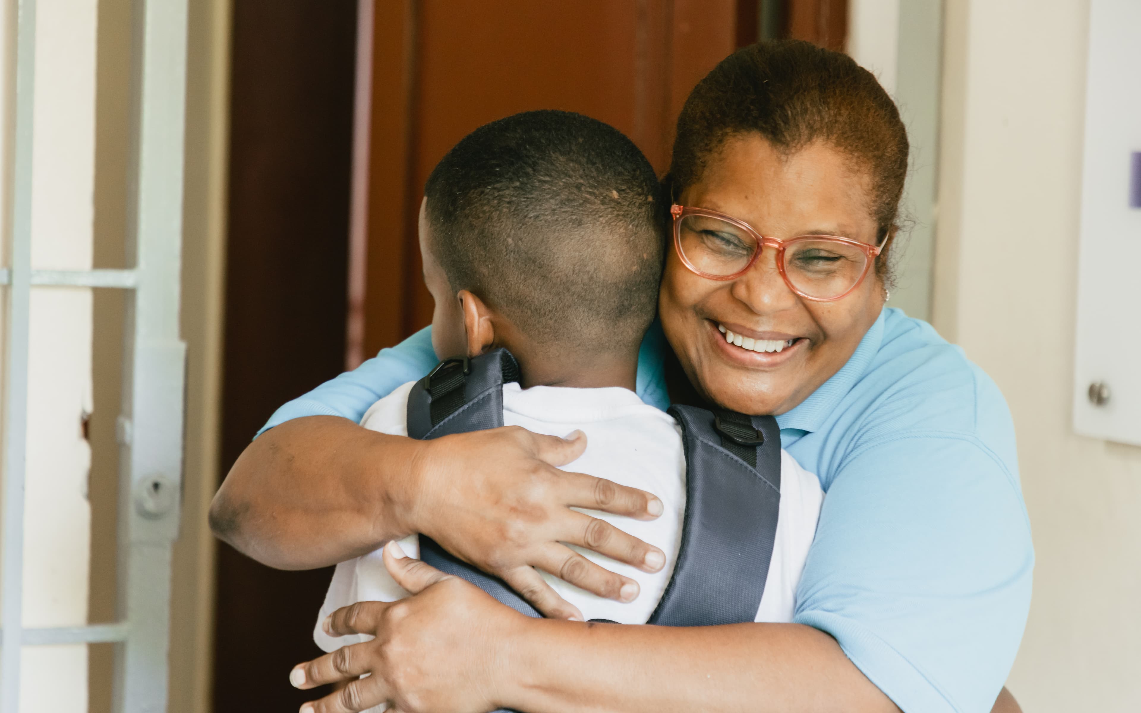A young boy wearing a backpack is hugged by an older woman.