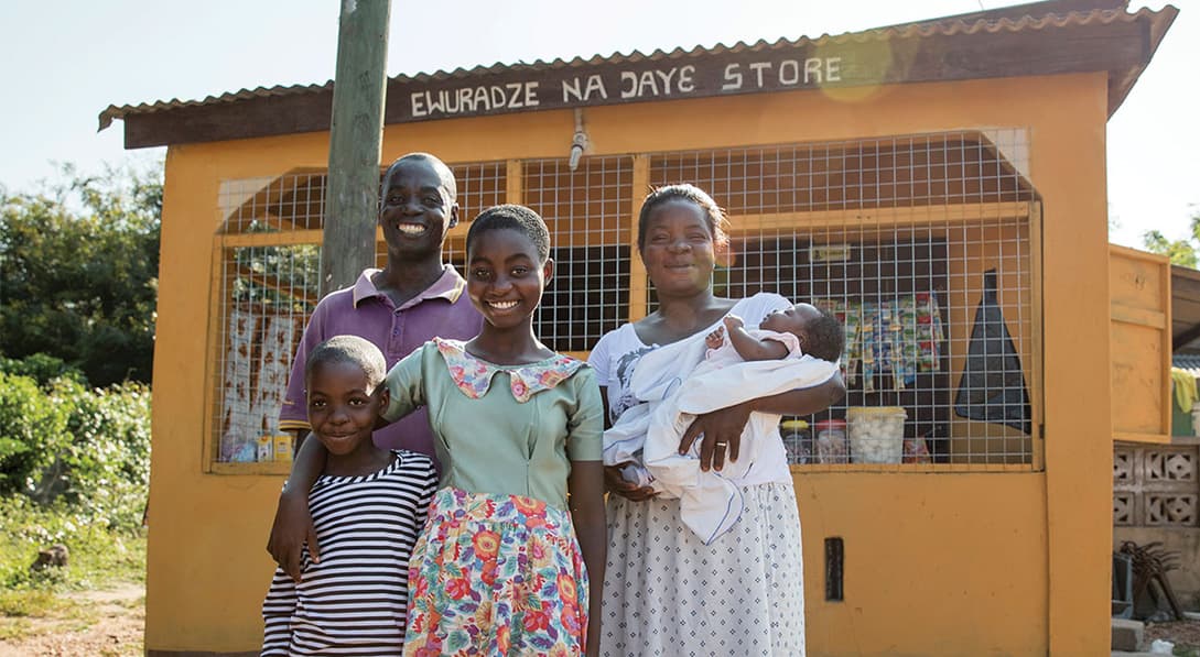 An African family stands in front of their yellow grocery store while smiling.