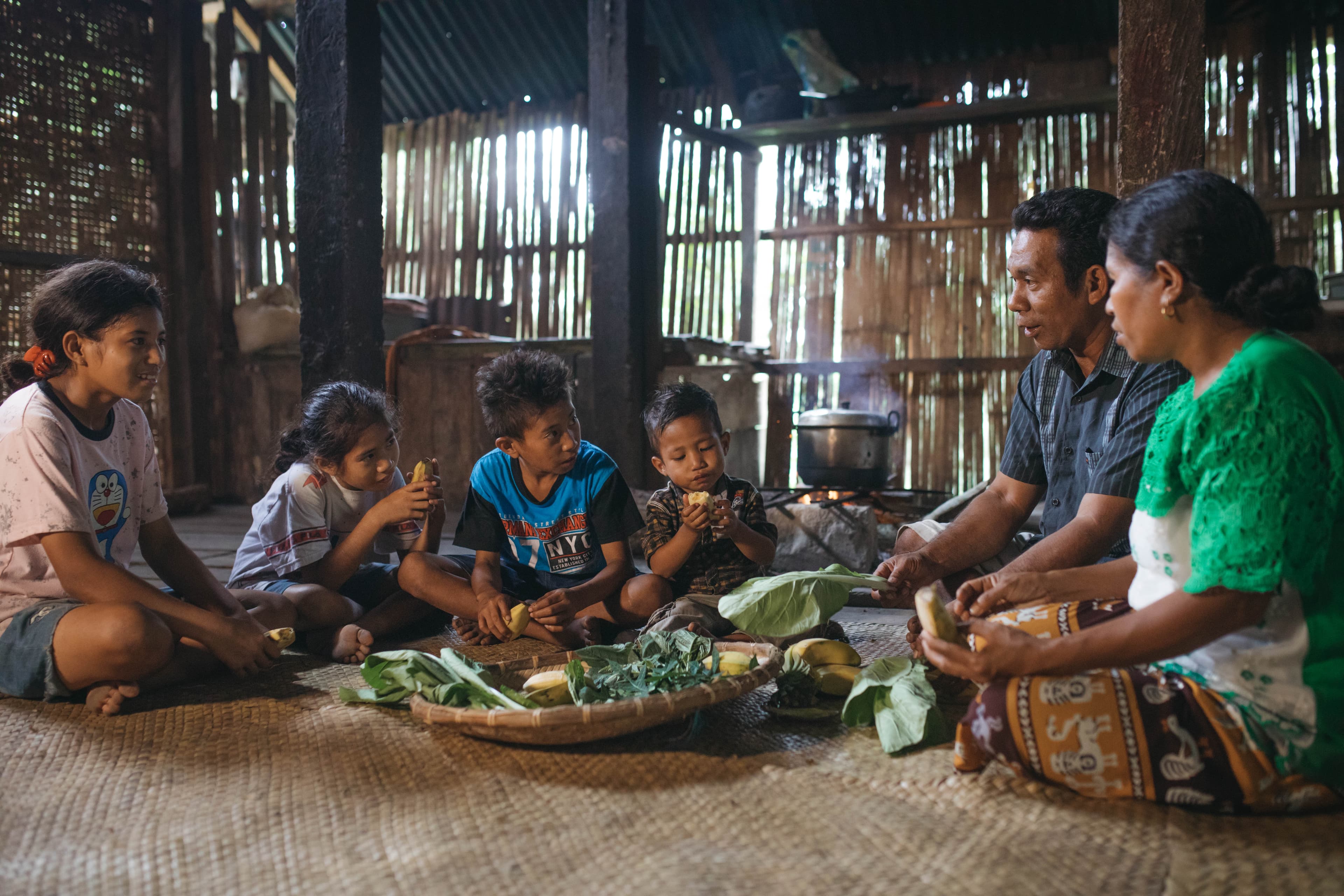 A family with young children sits on the ground with a tray of vegetables and fruits given to them by the Compassion center.