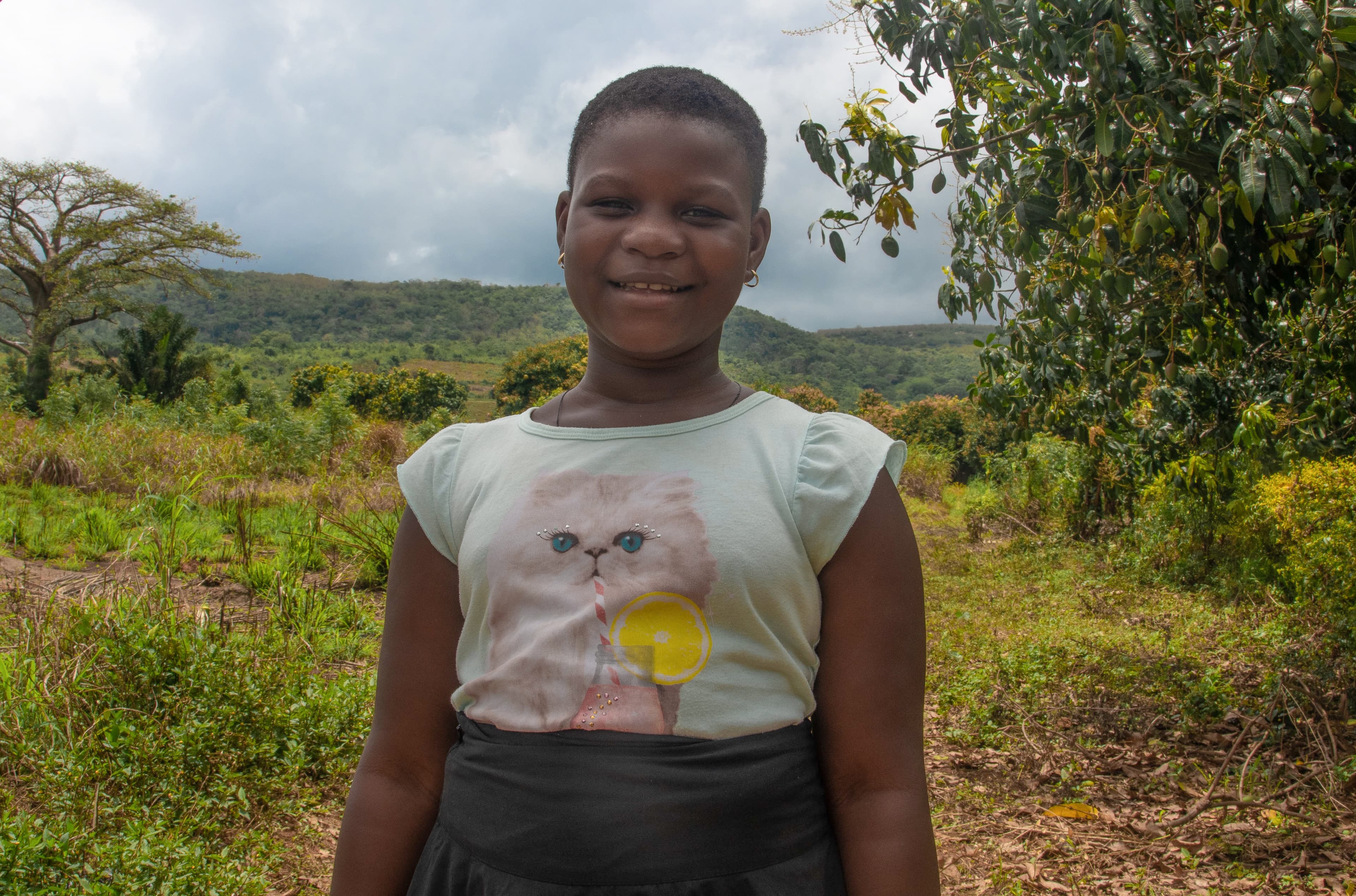 Young woman smiles and stands in front of greenery near her home.