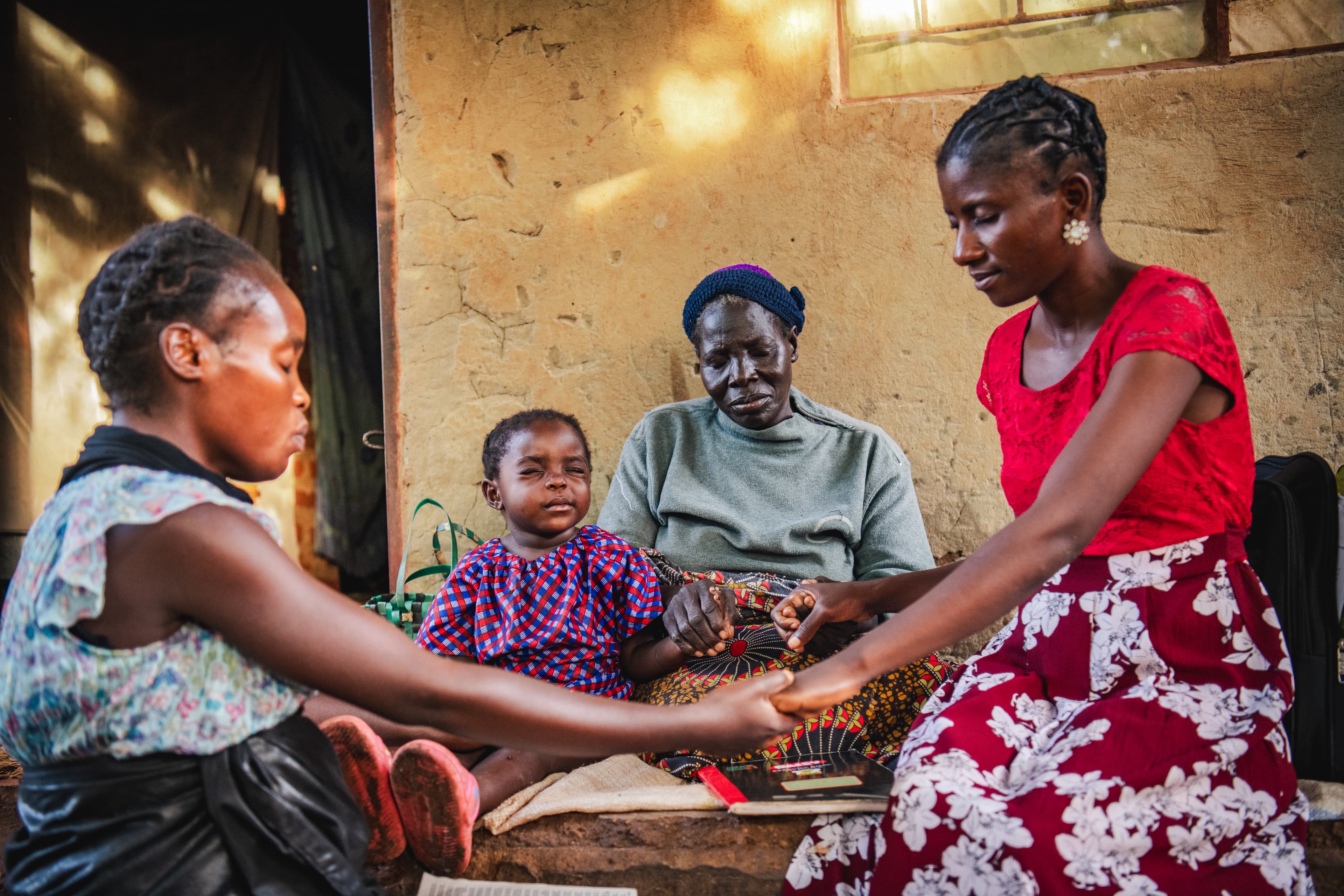 A group of African women hold hands and pray.
