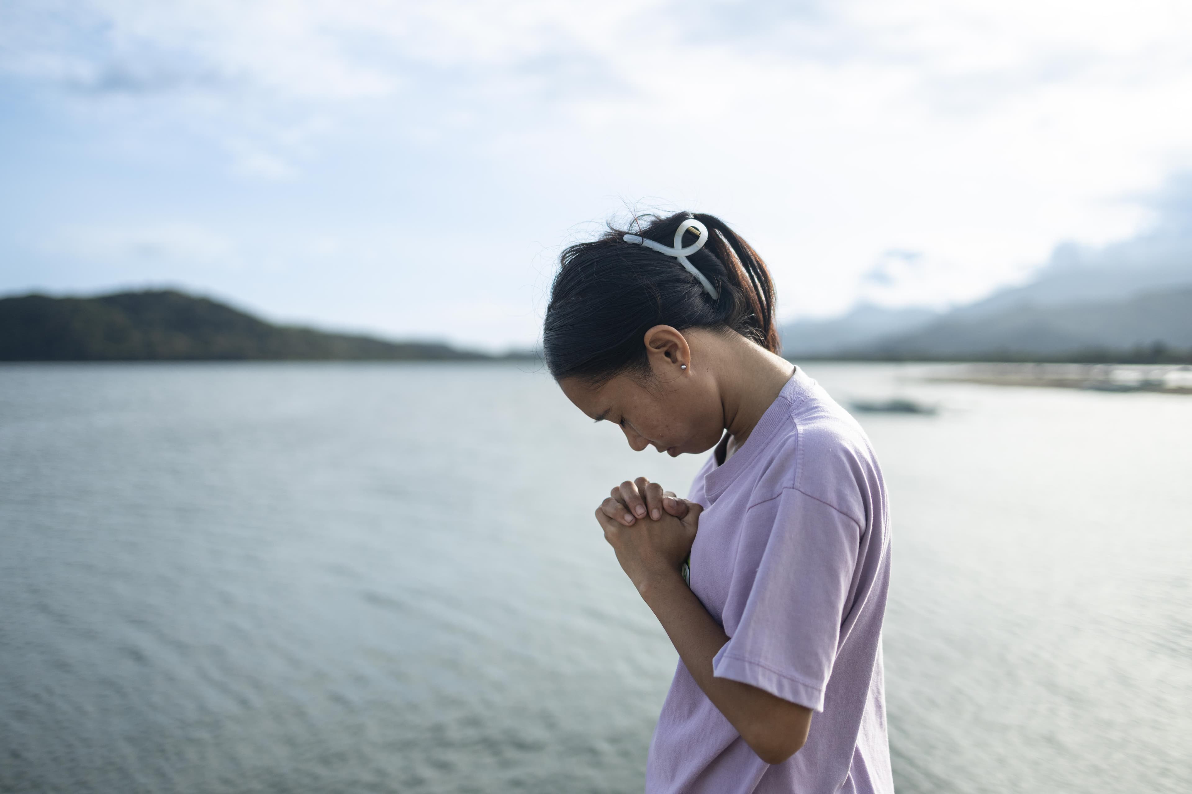 A young girl is bowing her head and has her hands clasped together in prayer.