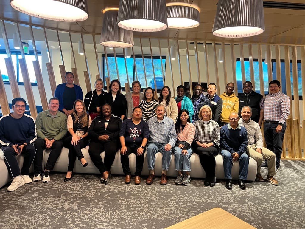 A group of adults sit on and stand around a couch while smiling for the camera.