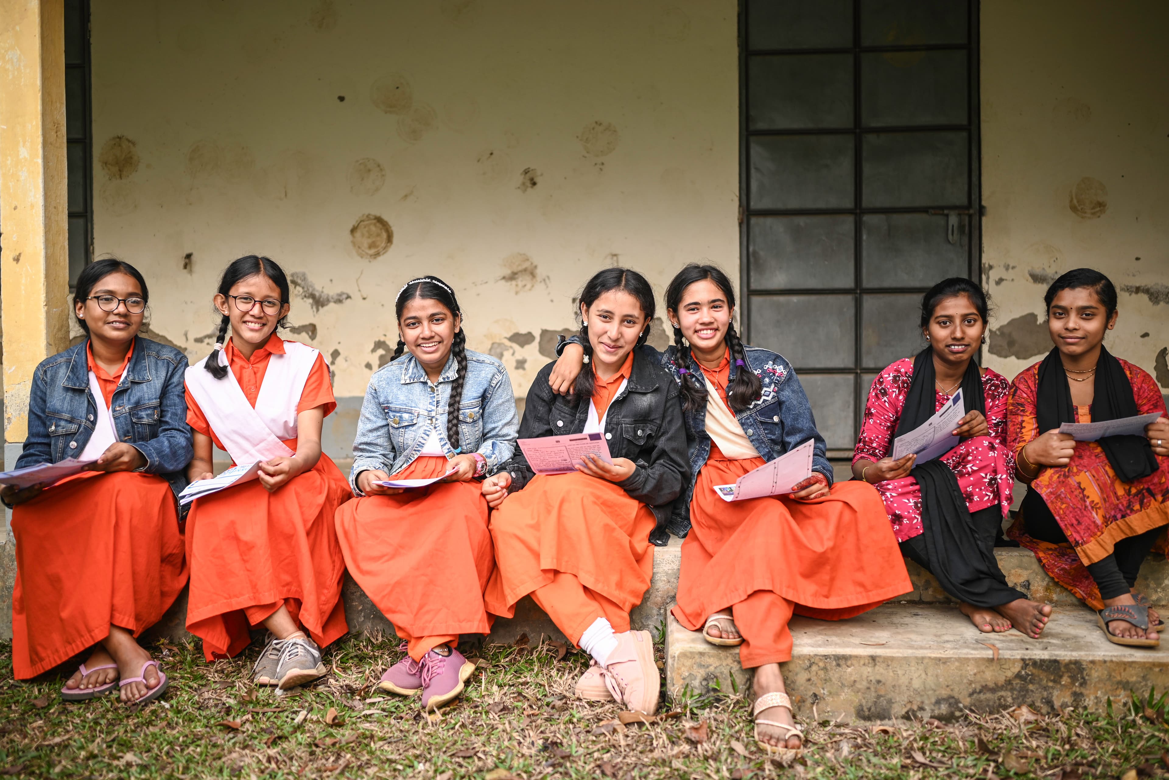 A group of girls are smiling as they sit, holding letters from their sponsors.