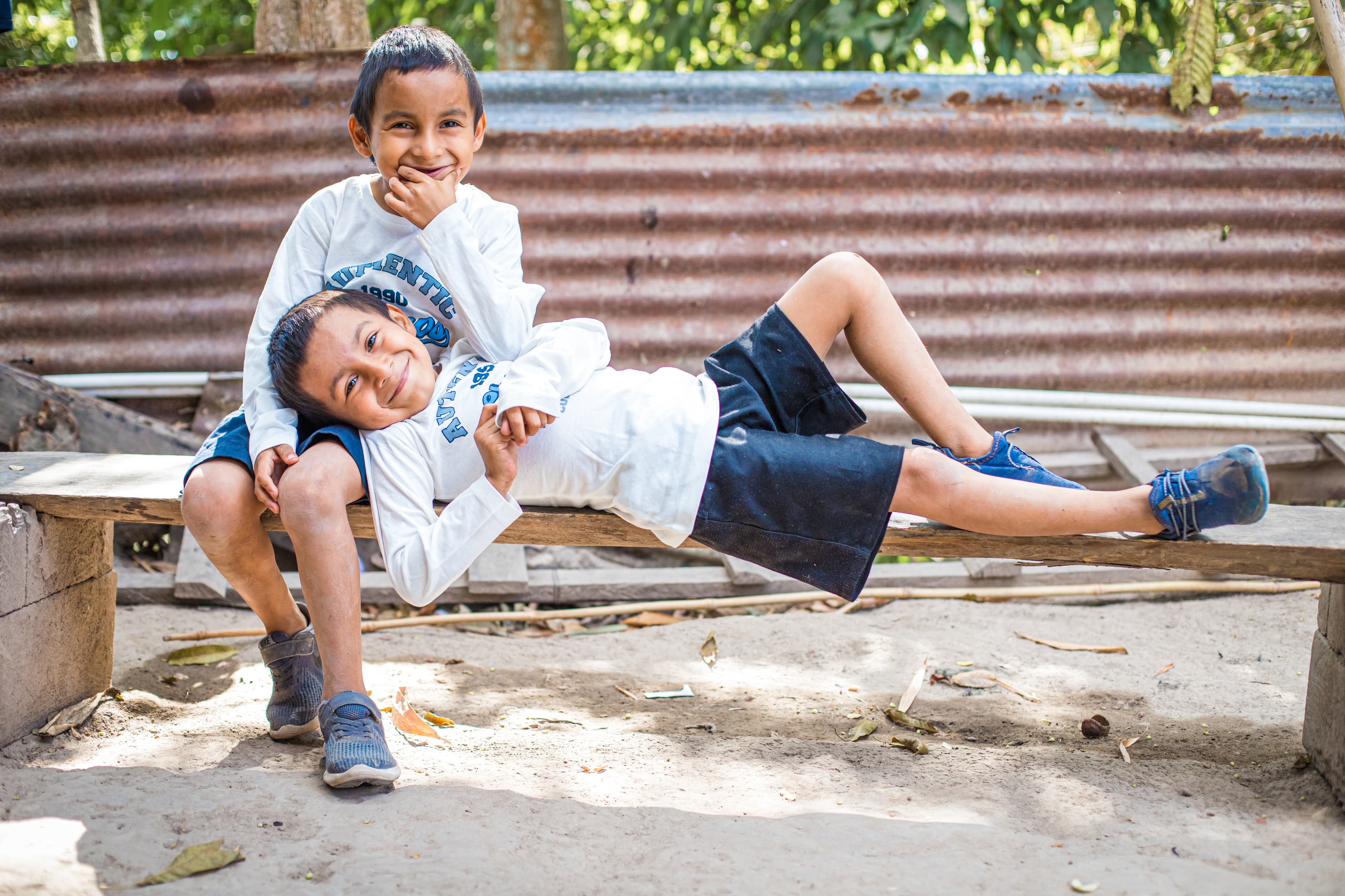 One young boy lays in the lap of another as they both smile for the camera.