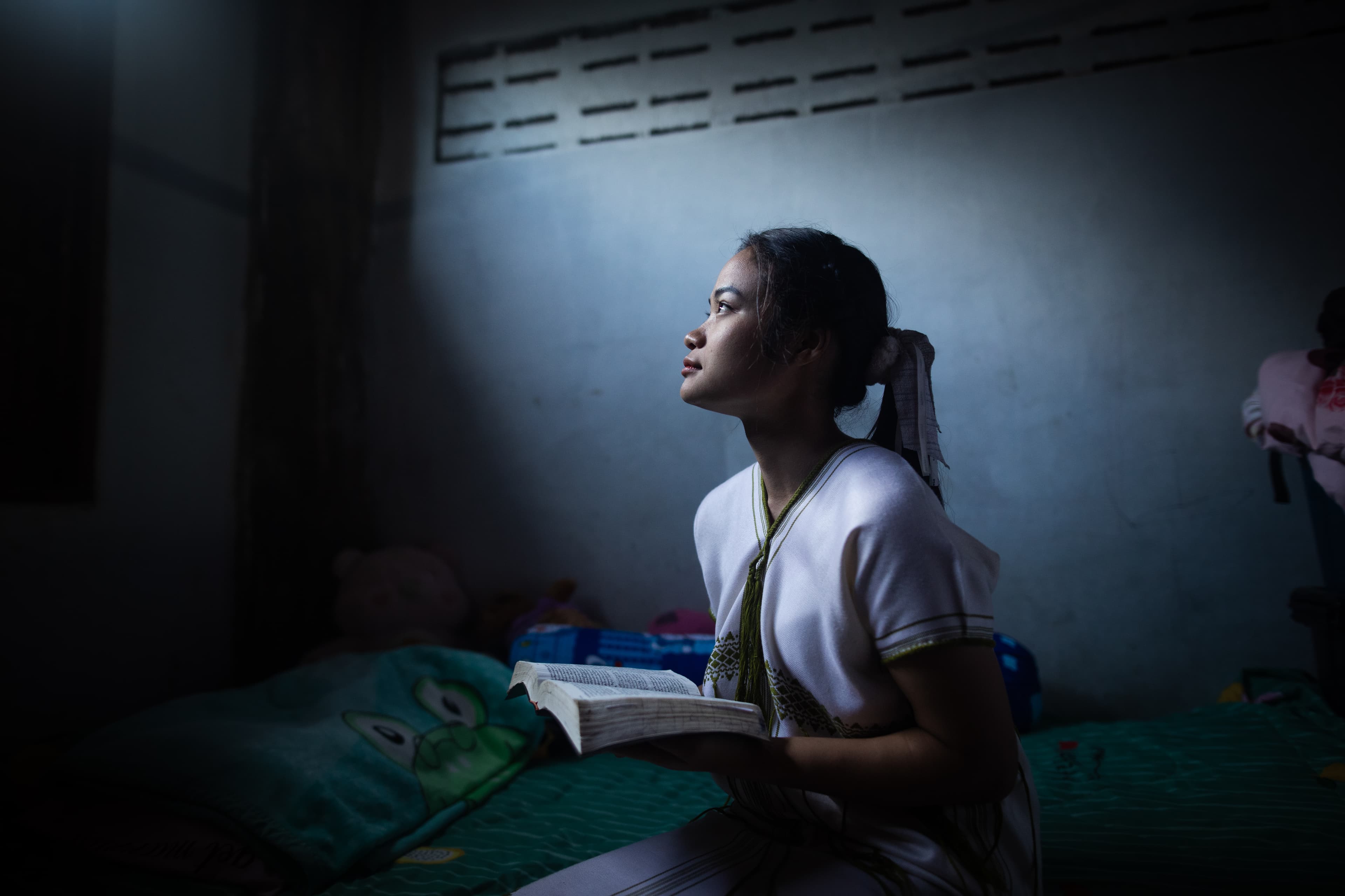 A young woman is holding her bible and looking up to her window as she prayers
