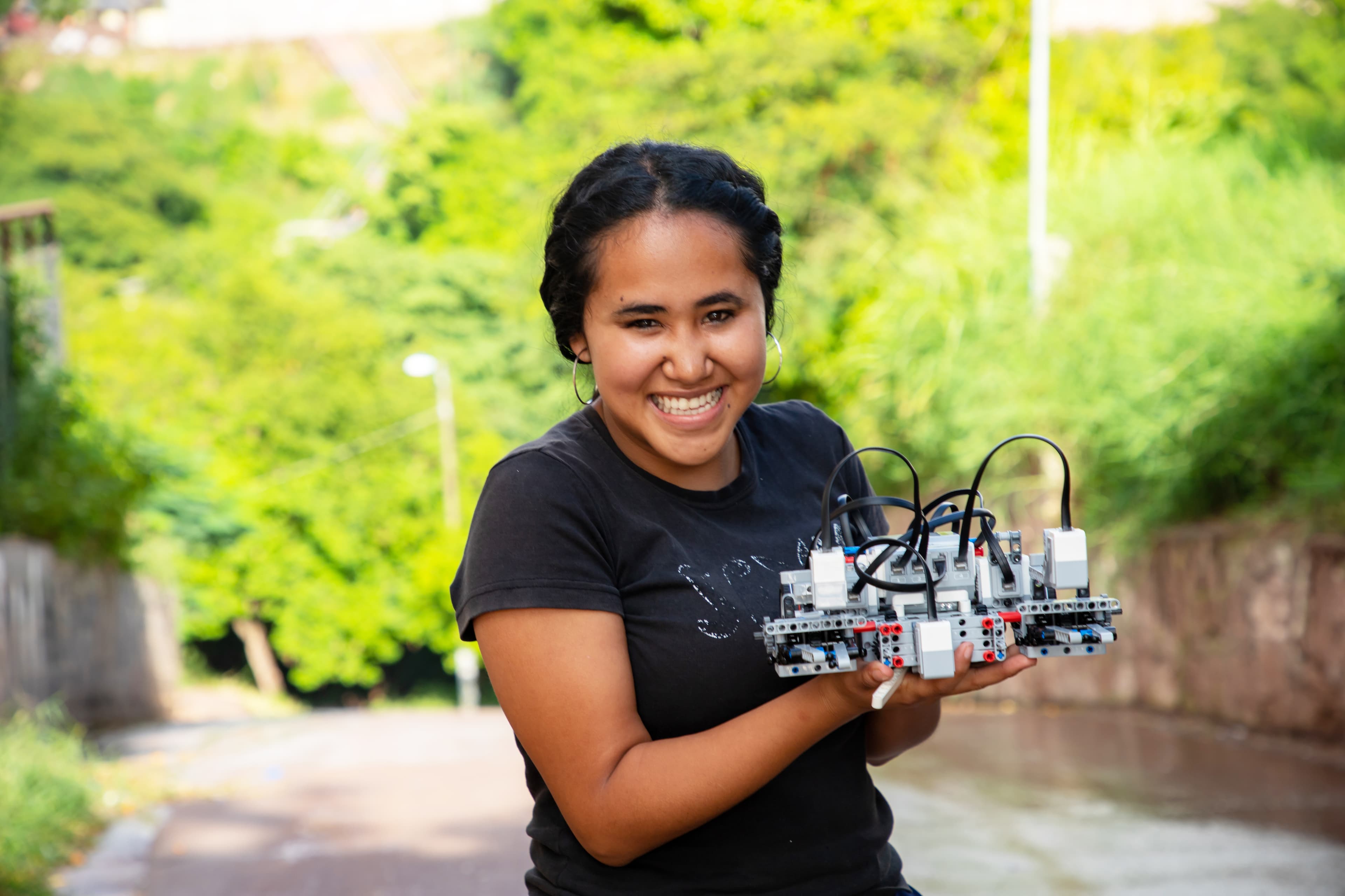 A teenaged girl smiles brightly holding robotics equipment.