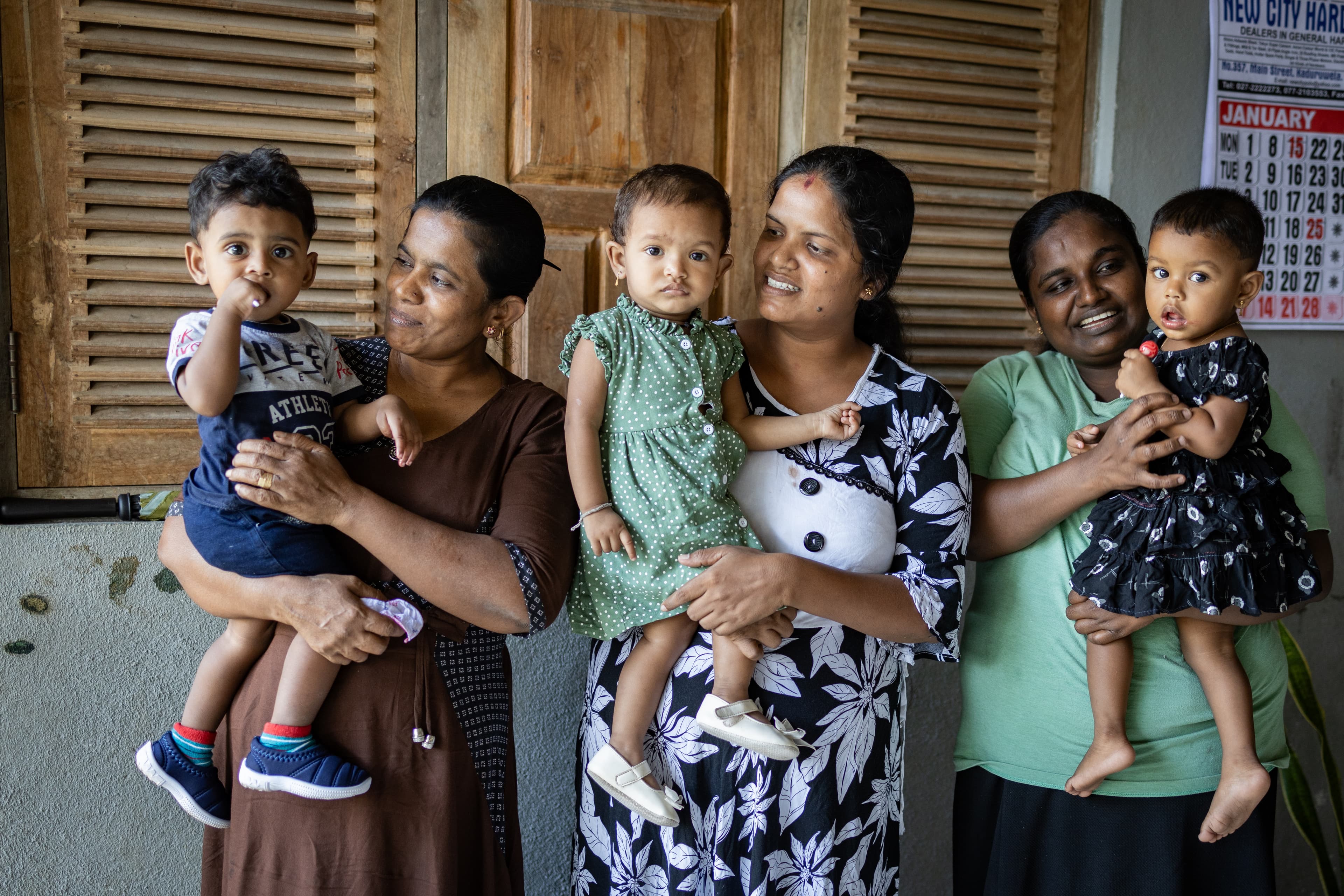 Three moms hold their toddler children as they smile.