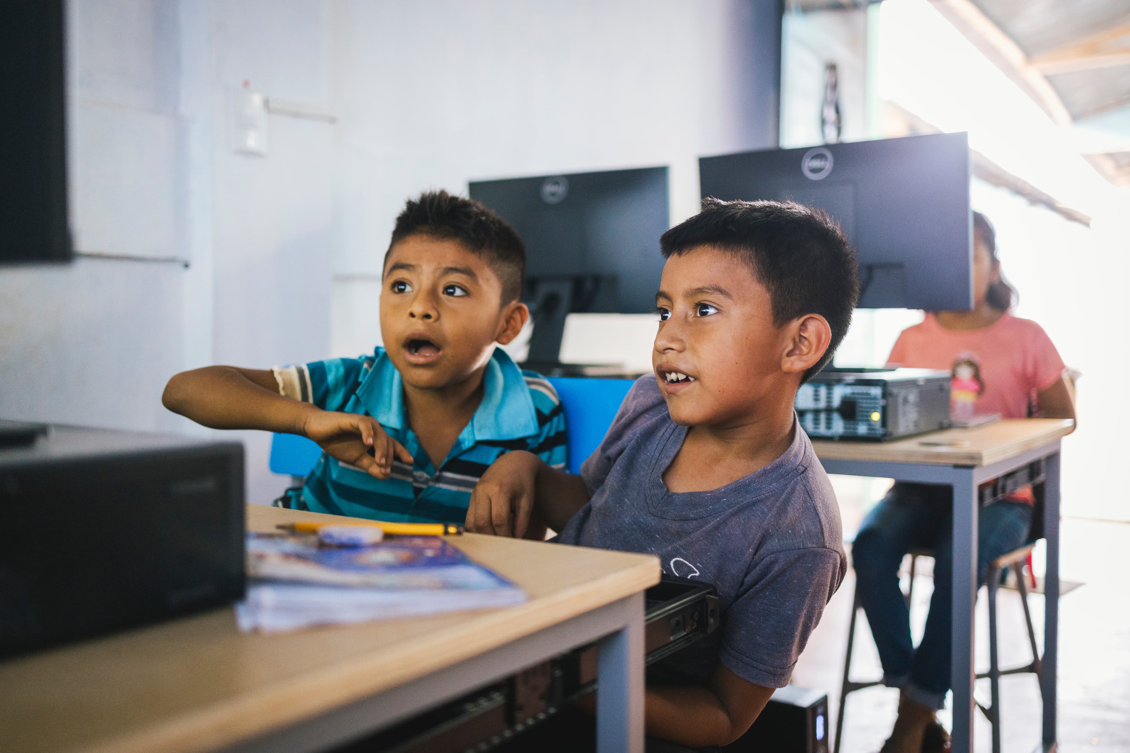 Two young boys smile while looking at a computer.