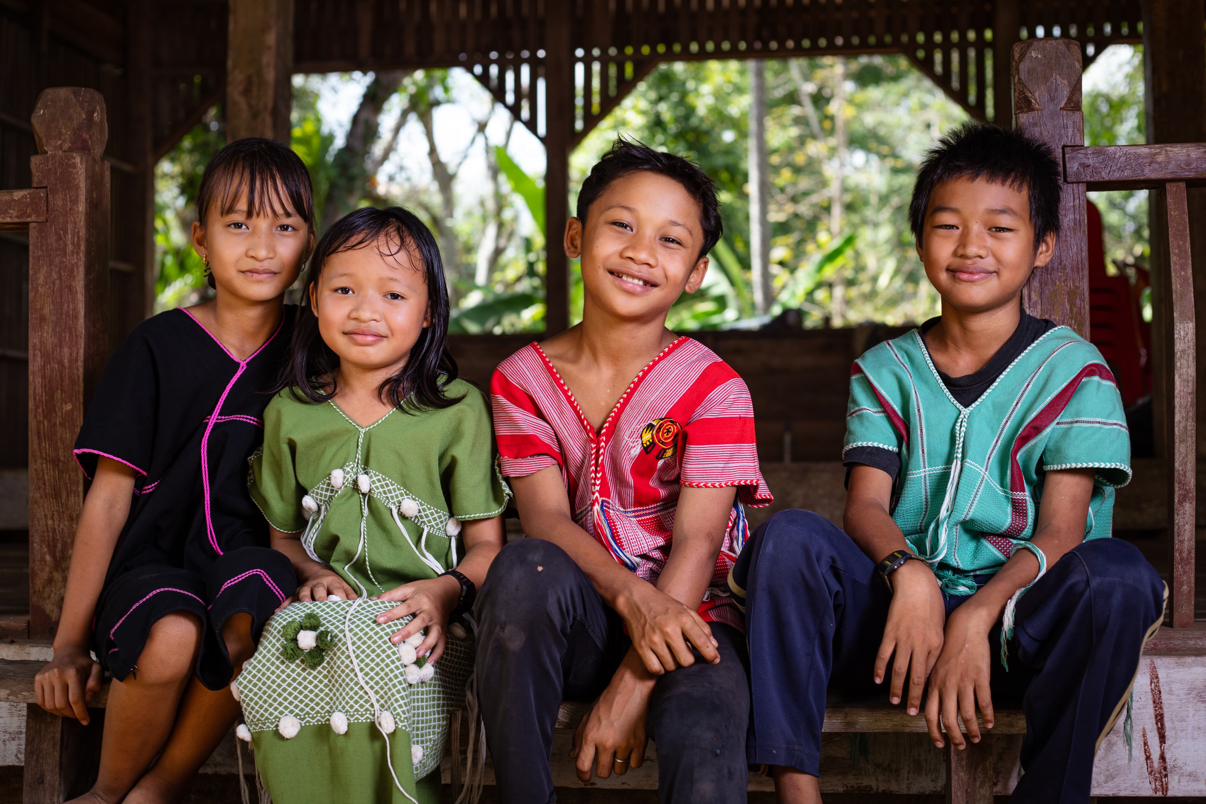 Four children are sitting together on a bench looking at the camera.