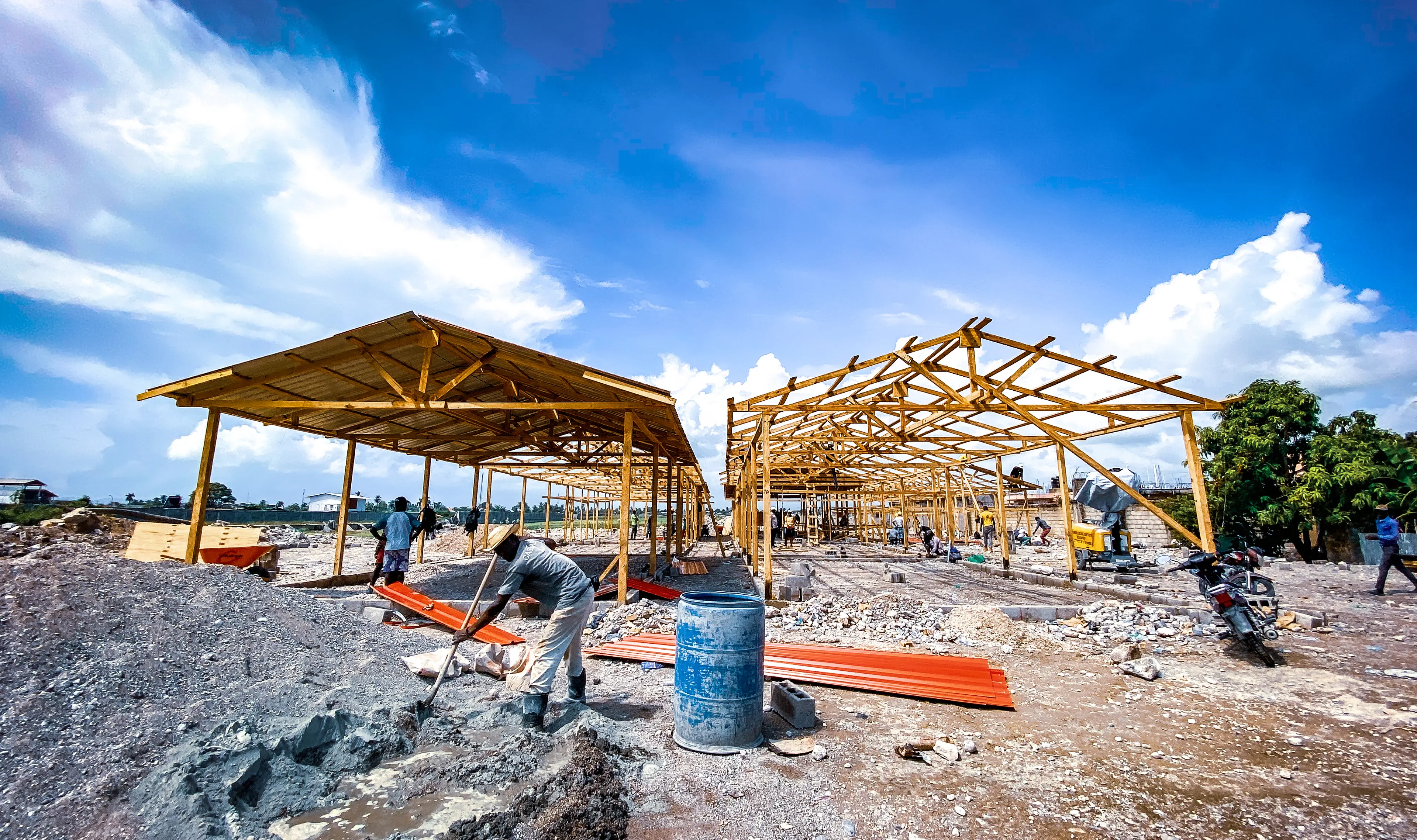 Wooden building frames stand in front of a bright blue, cloud-filled sky.