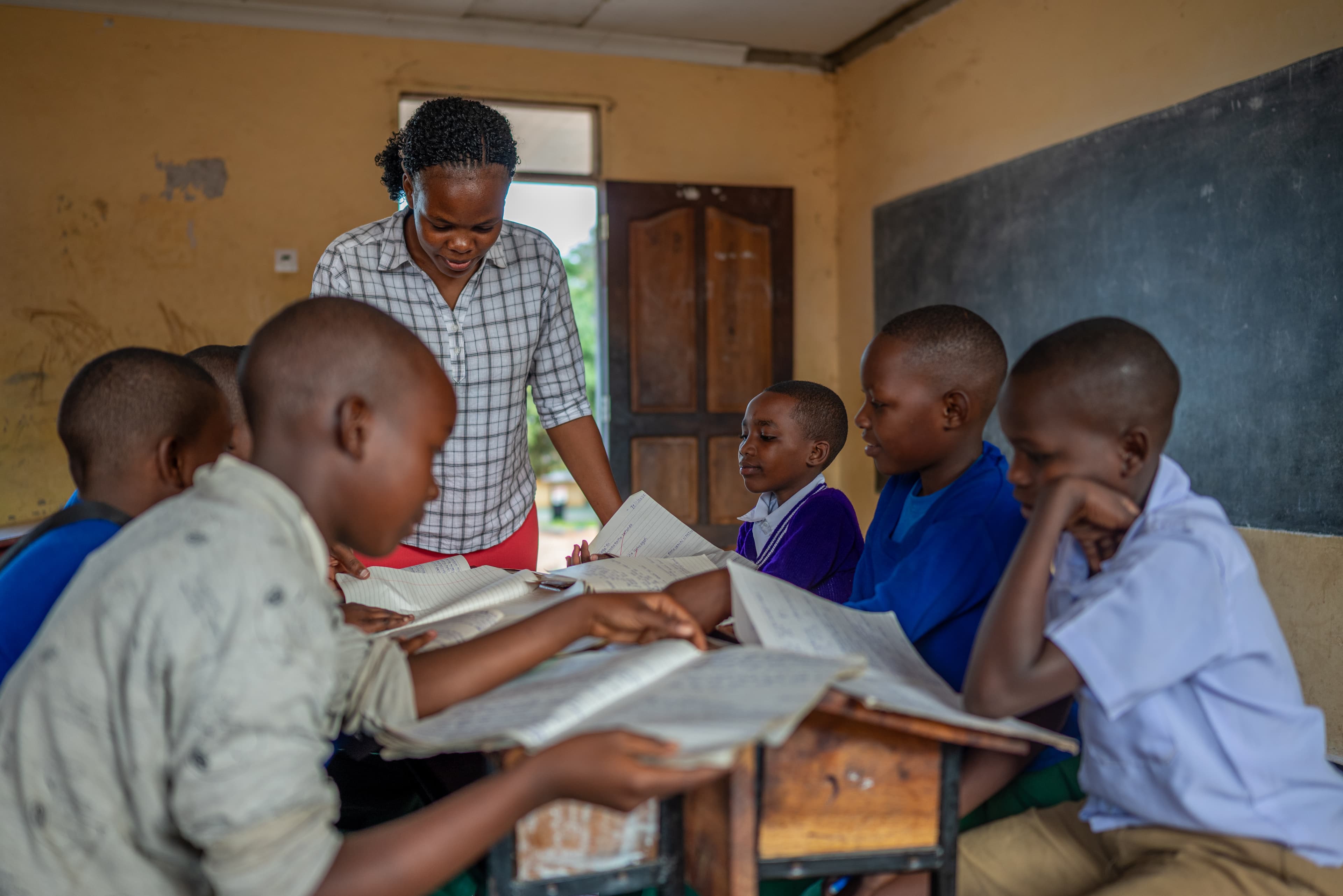 A group of African children sit at desks while reading from workbooks.