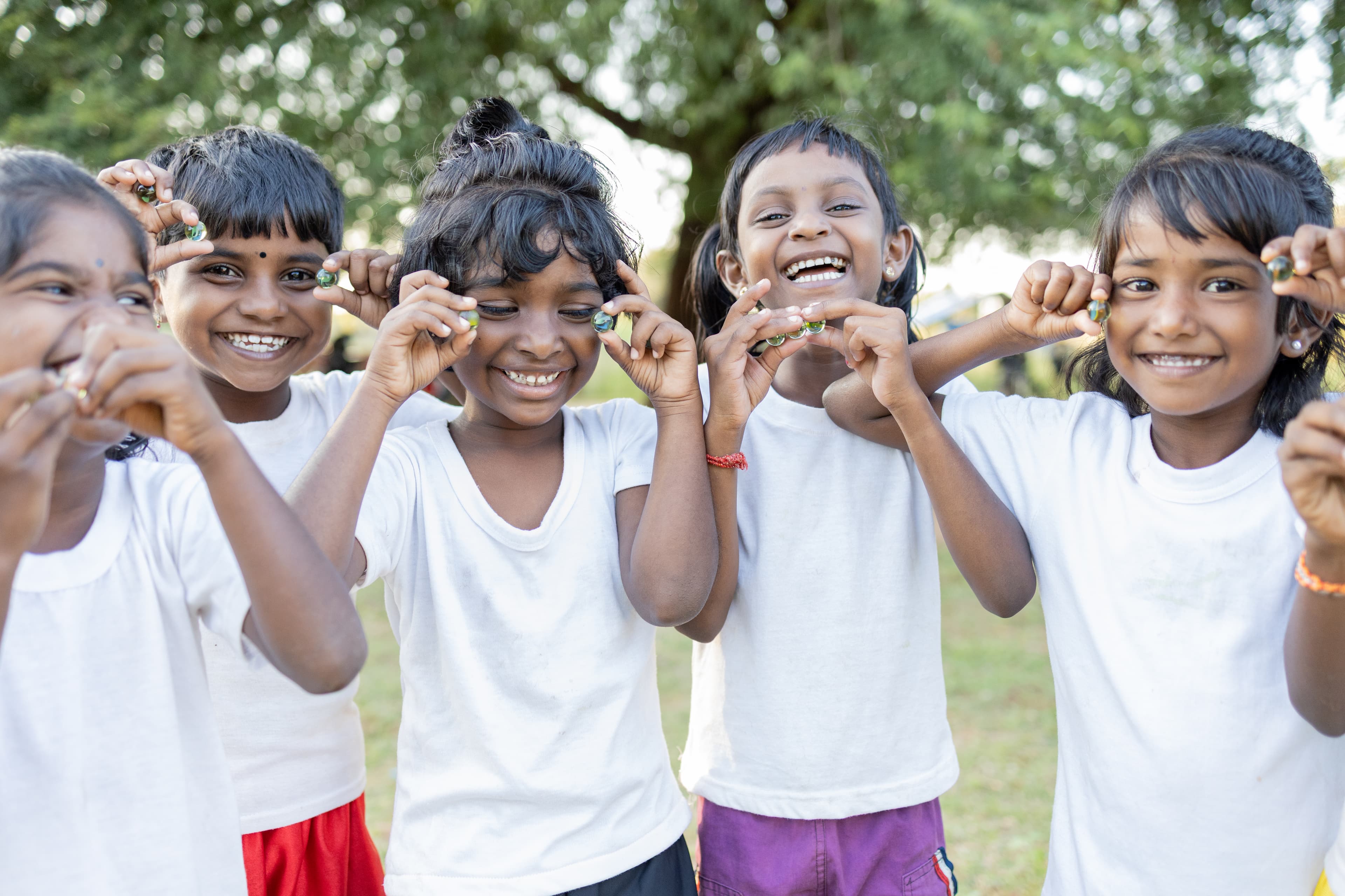 A group of young children are standing together, smiling and holding marbles in their hands as they play at the local child development center.