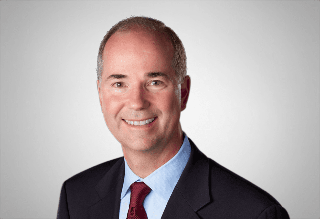 Chris Knepper is in a blue shirt, red tie and black suit jacket is smiling, with a grey background behind him.