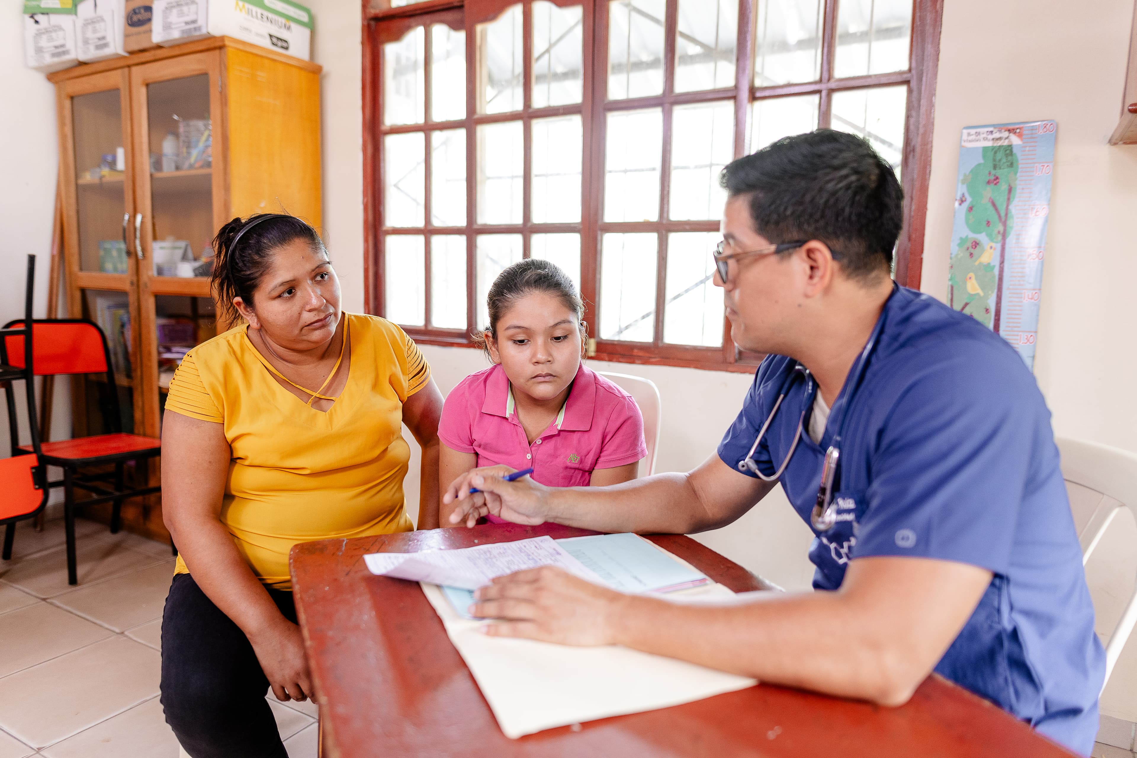 A mom and young girl sit at a desk with a doctor.