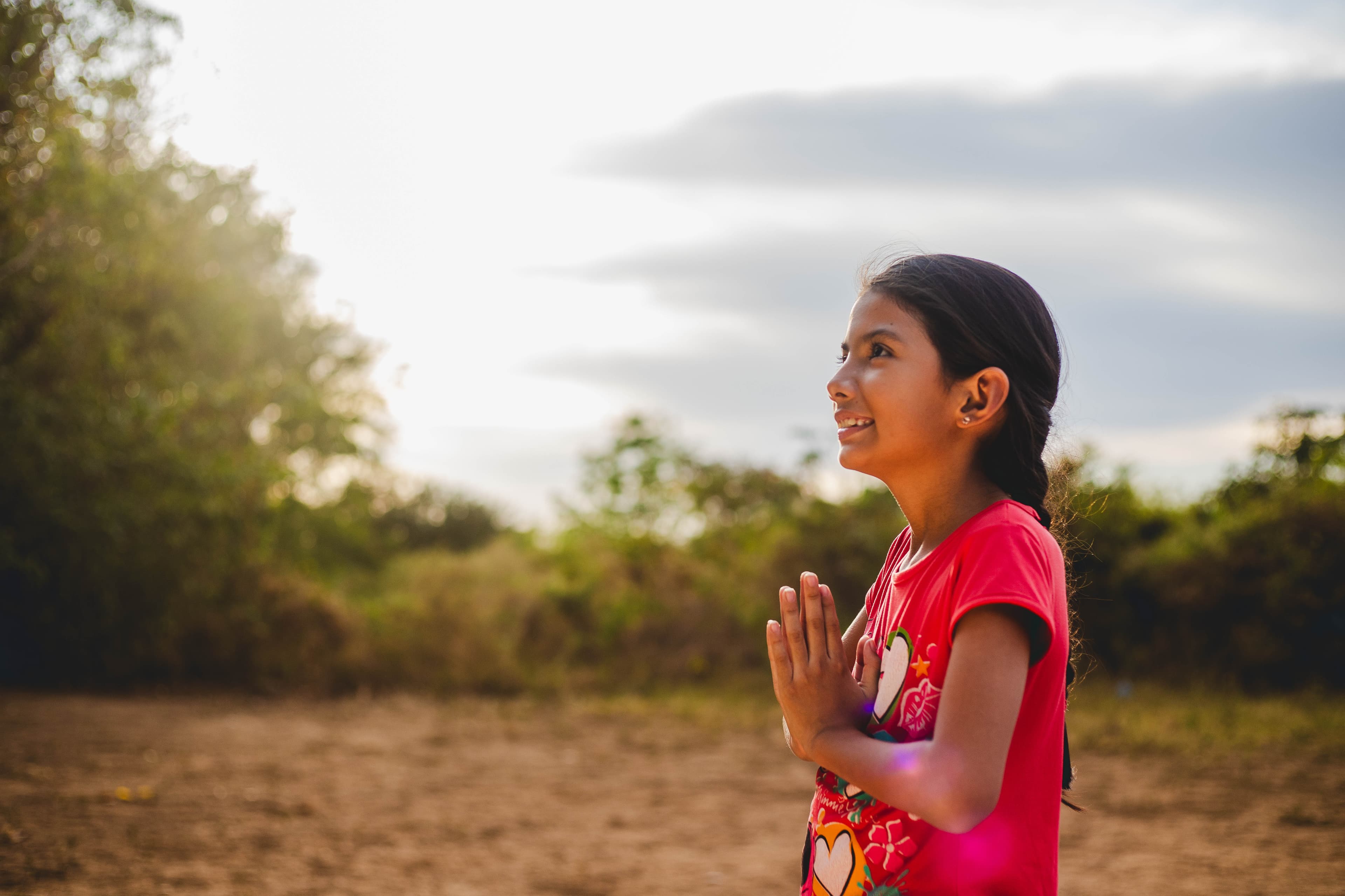 A young girl holds her hands together in prayer while looking up to the sky.