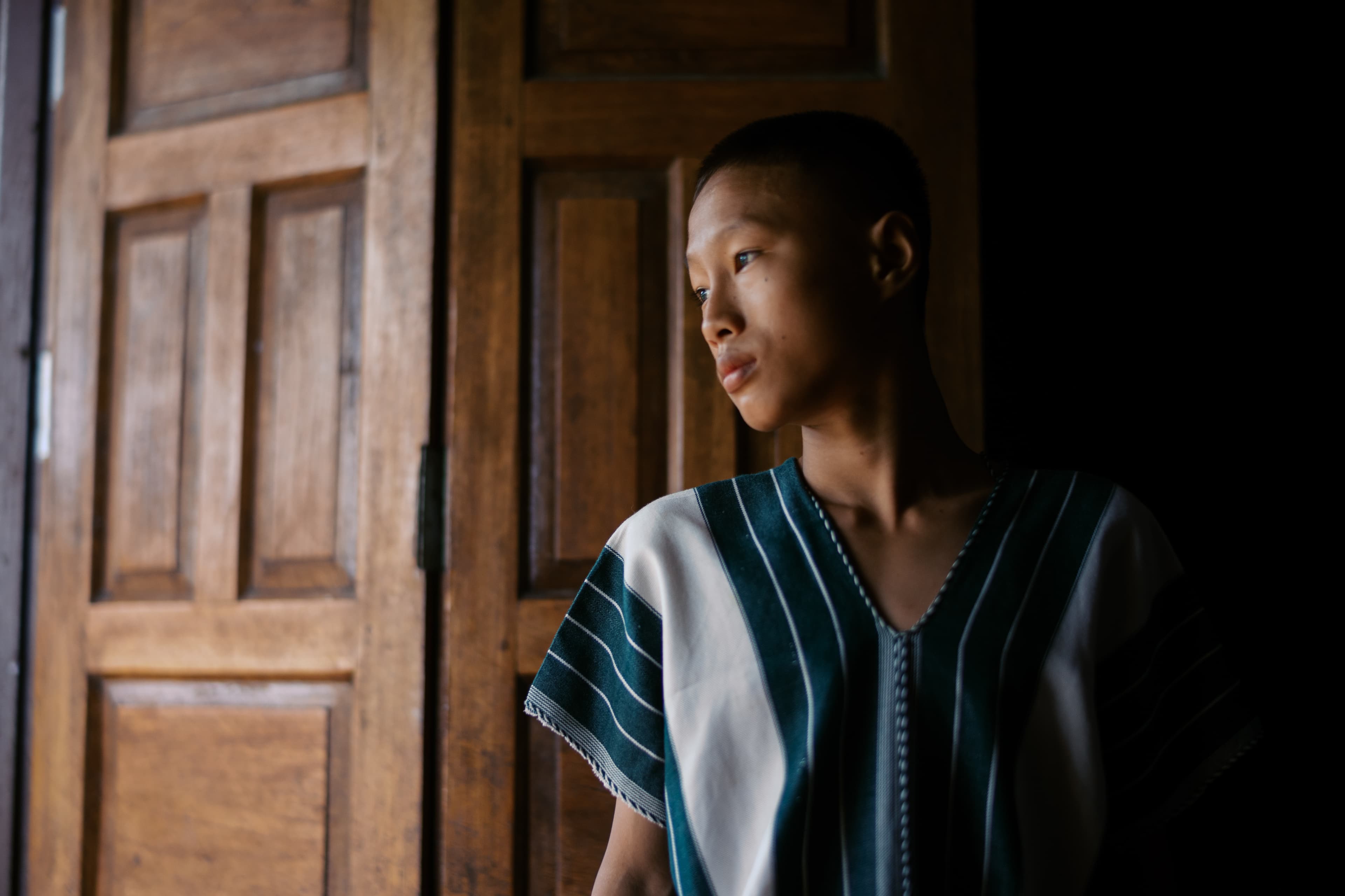 A boy stands with his back against a door, looking outside.