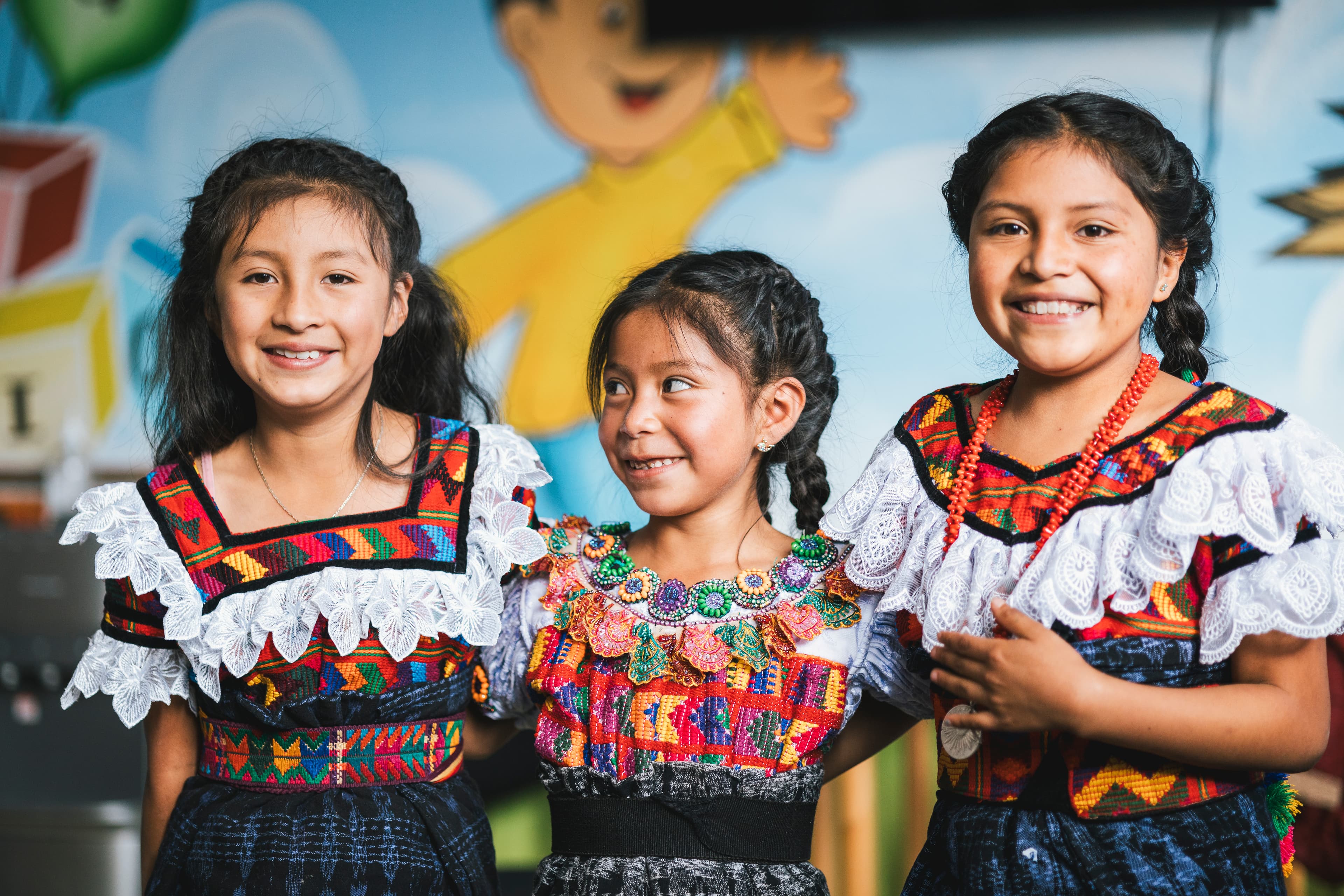 Three young girls smile and stand together in colorful clothes.