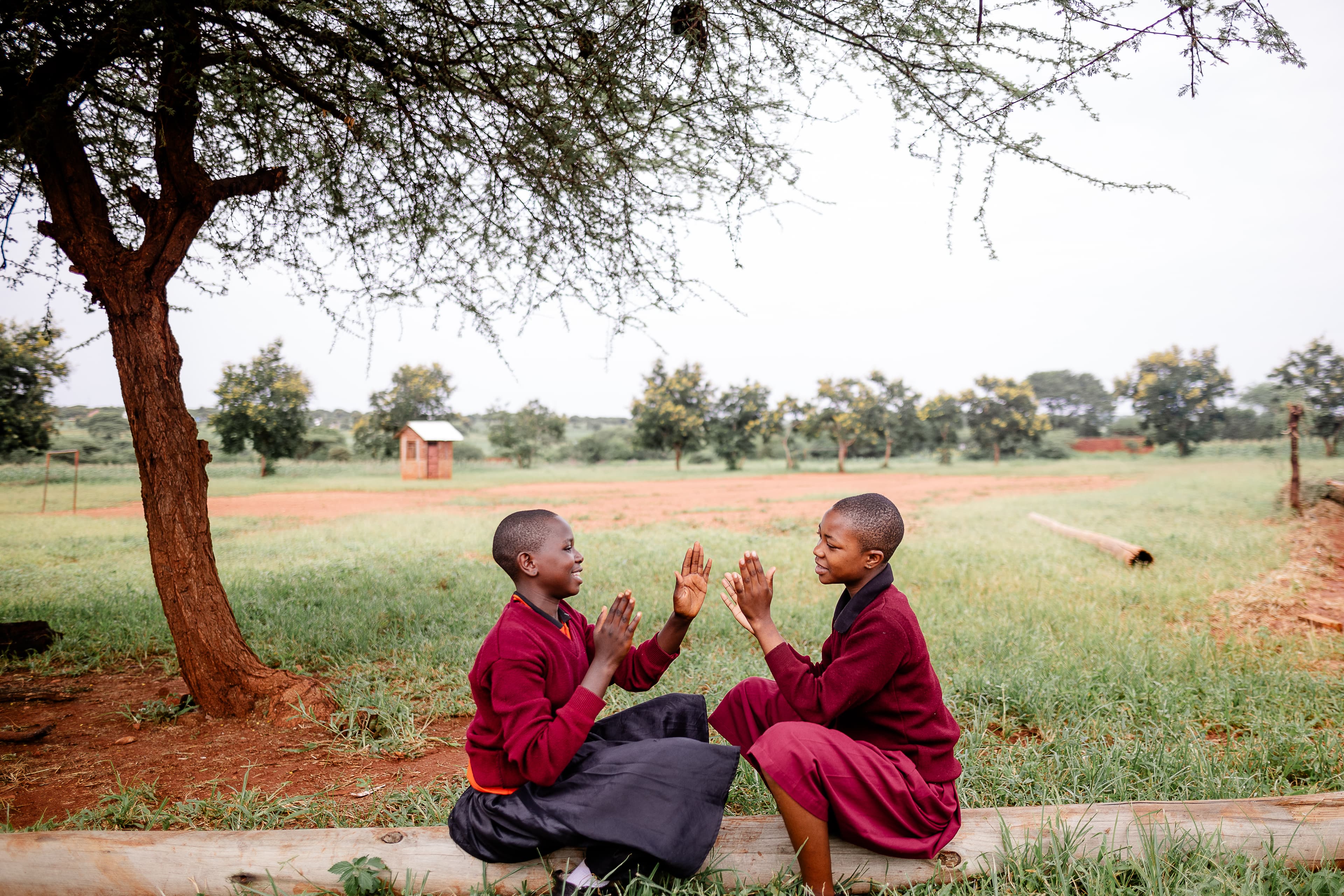 Two young women are playing games as they sit outside on the sidewalk.