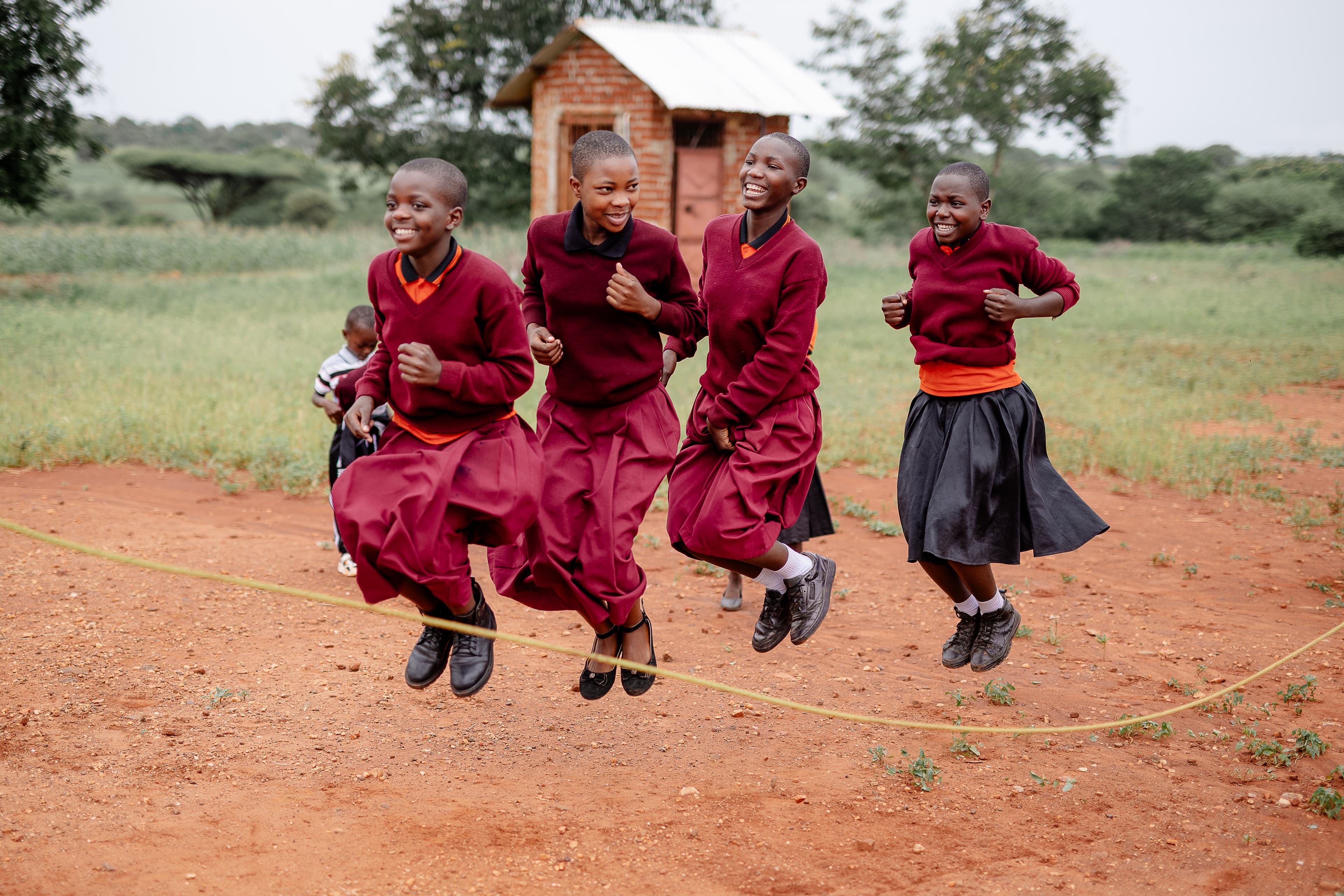 Four girls with matching red sweaters, skirts and joyful expressions on their faces jump over a rope outdoors