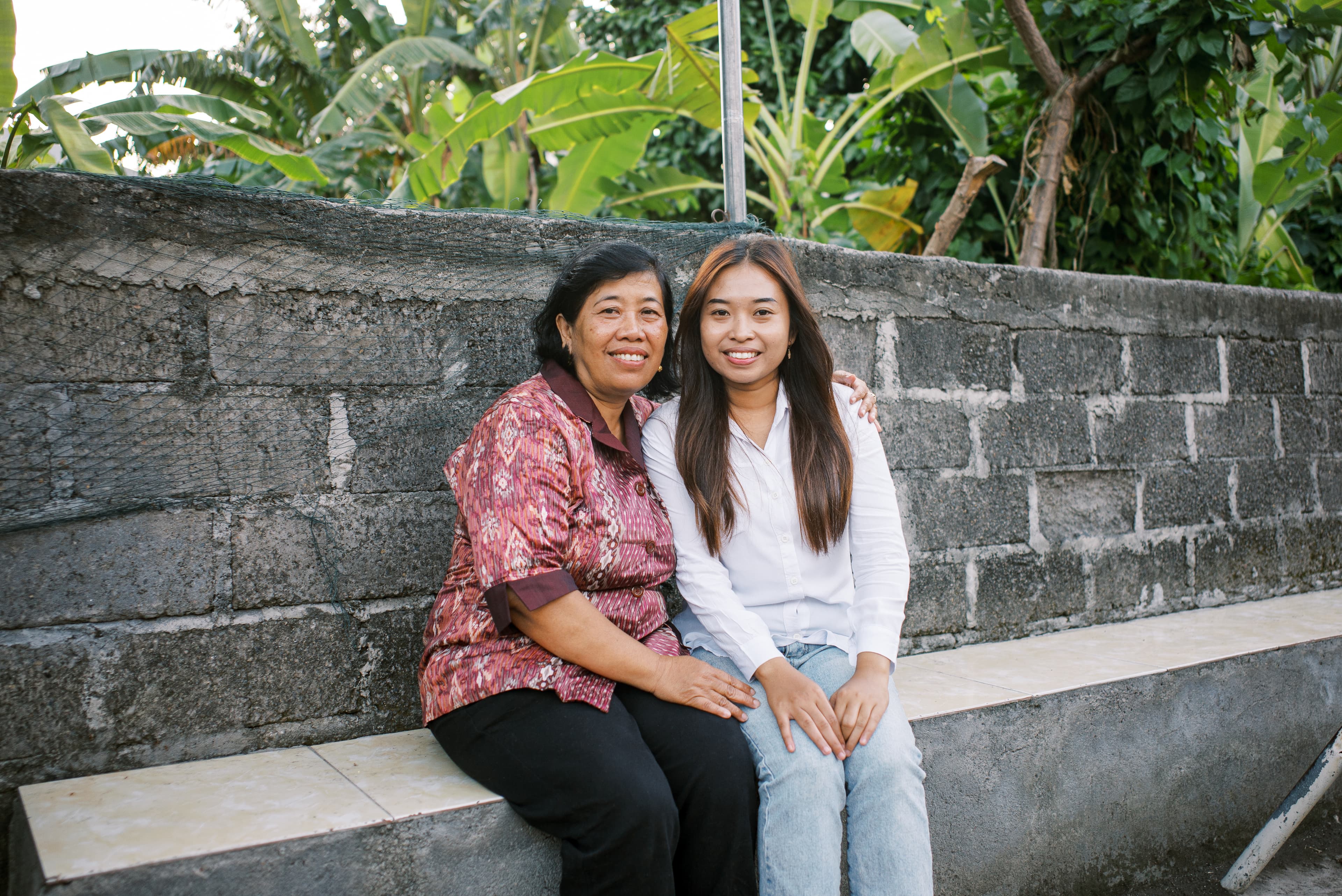 An older Indonesian woman sits next to a teen girl as they smile for the camera.