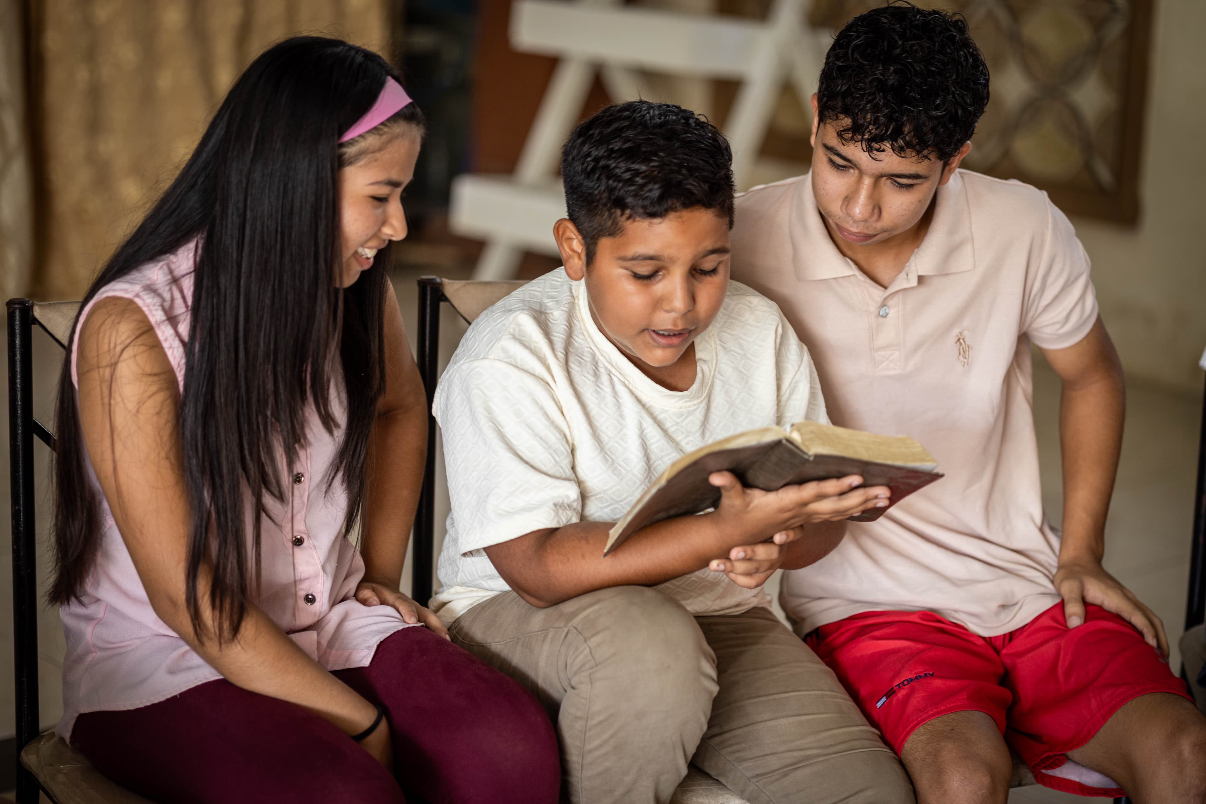 Three teens sit and read a Bible together while smiling.