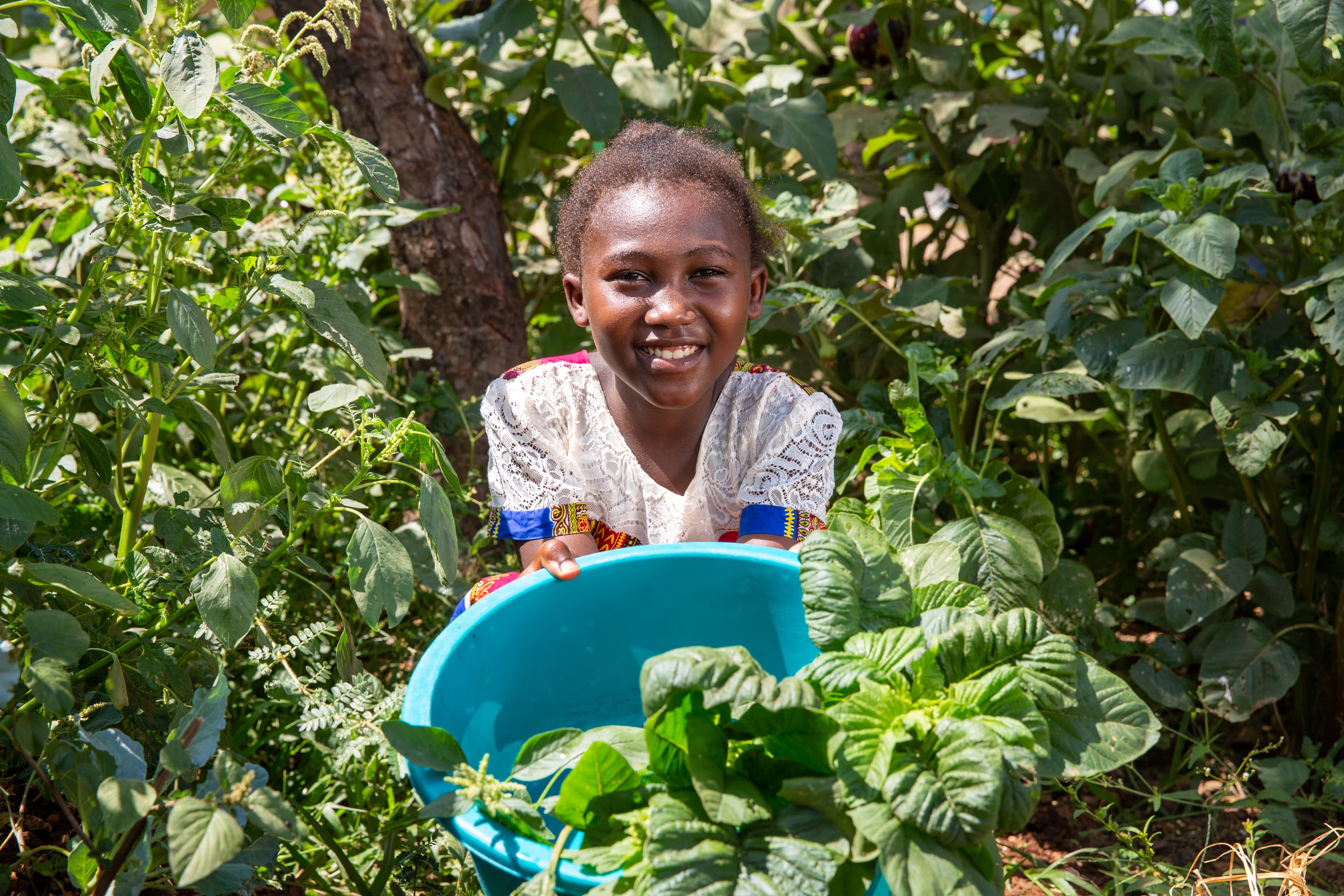 A young girl is smiling as she holds up greens from her family’s garden.